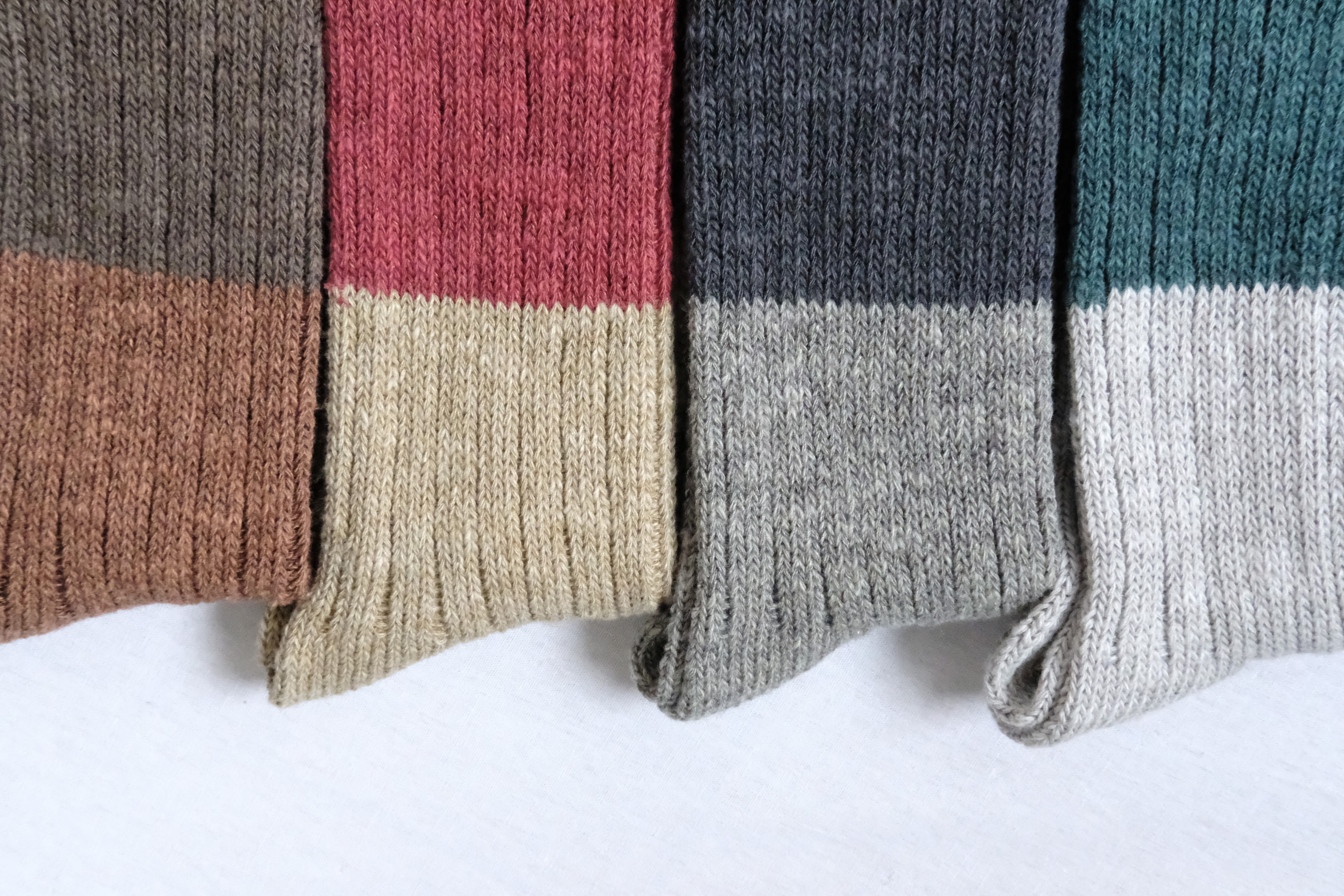 Four pairs of ribbed socks in brown, red, gray, and green, each with a contrasting lighter-colored cuff.