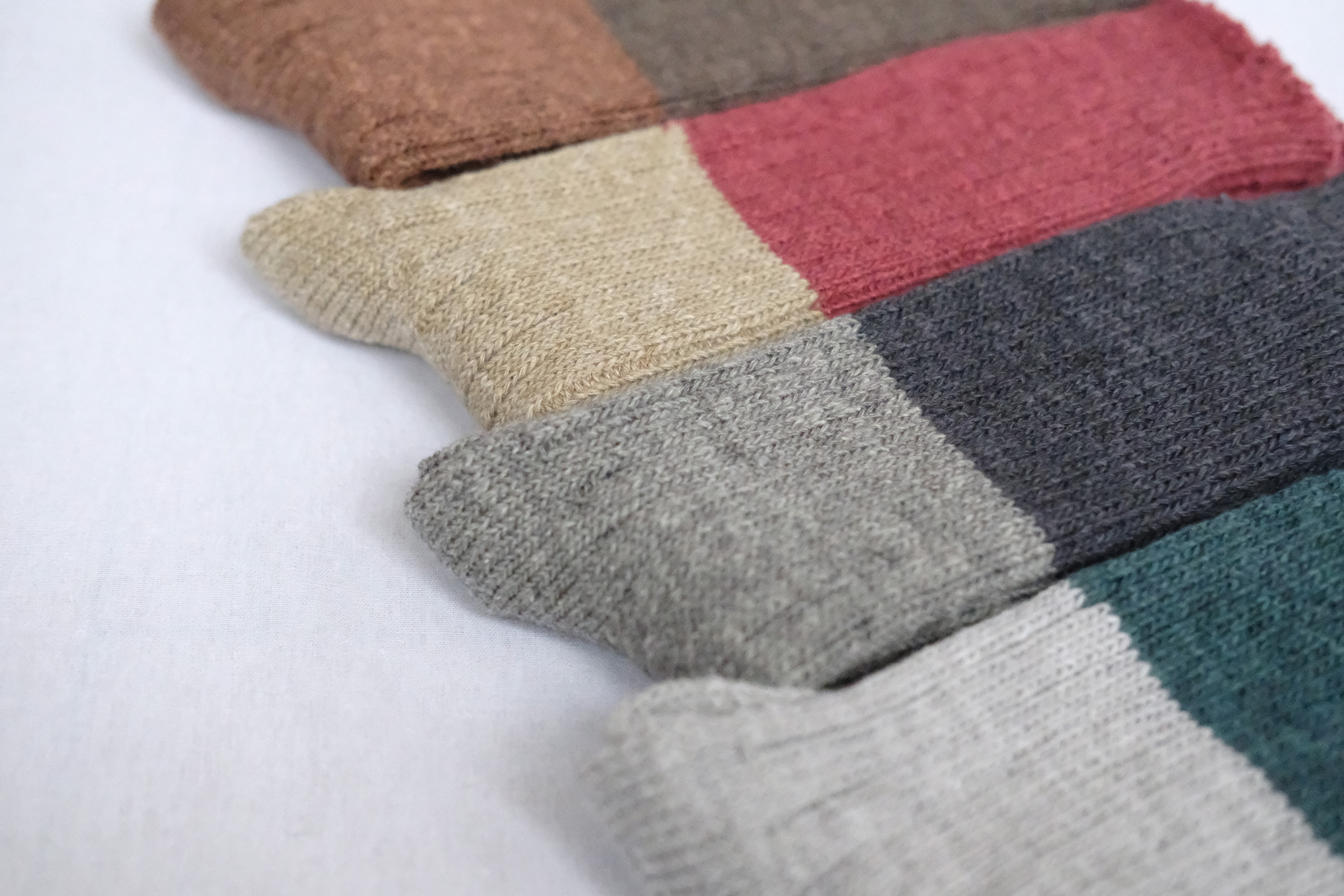 Five pairs of knit socks in brown, beige, burgundy, gray, and teal.  Each sock features a two-tone color block design.
