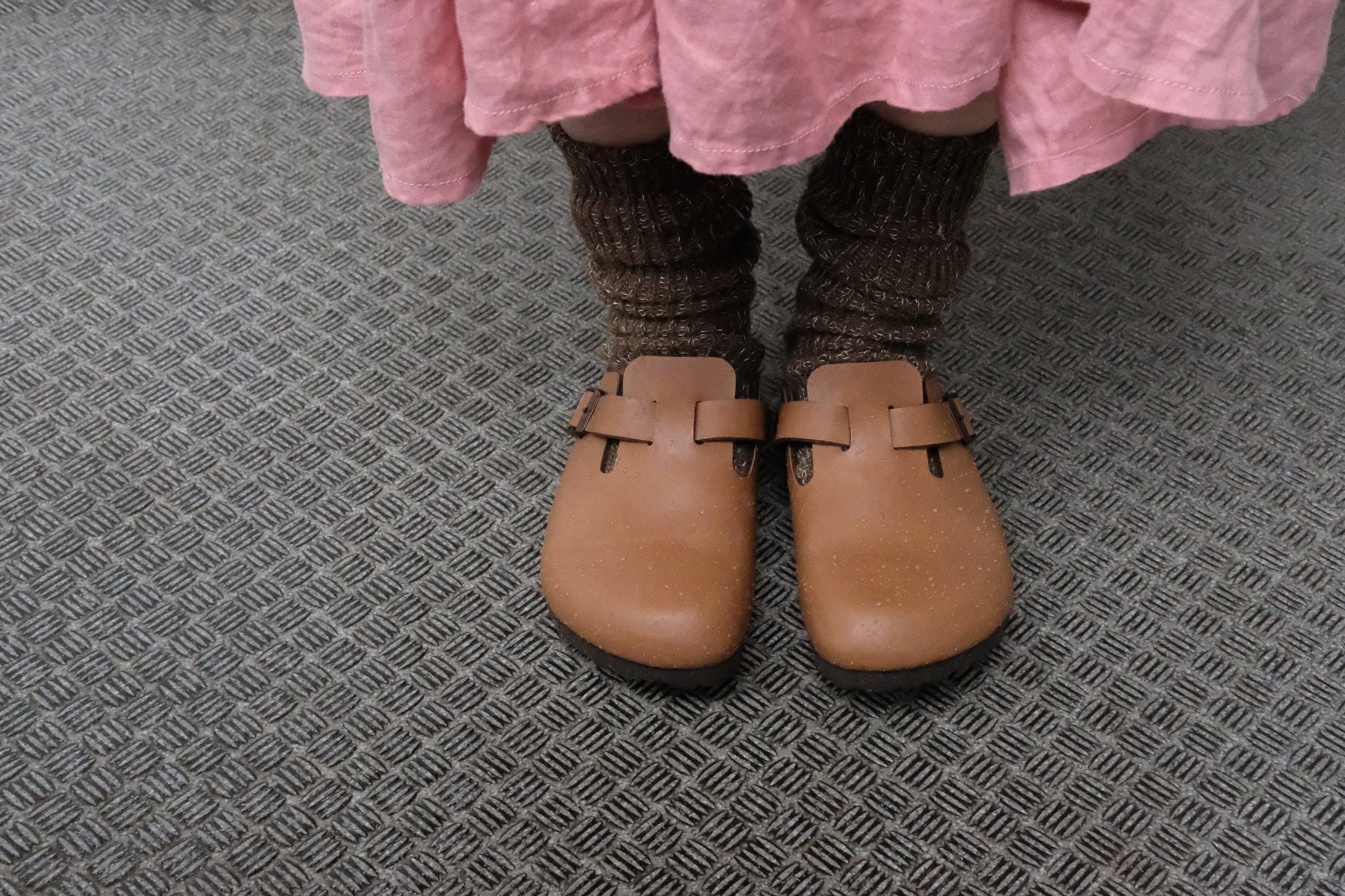 Pair of light brown leather clogs with single buckle straps, worn with brown knitted socks.