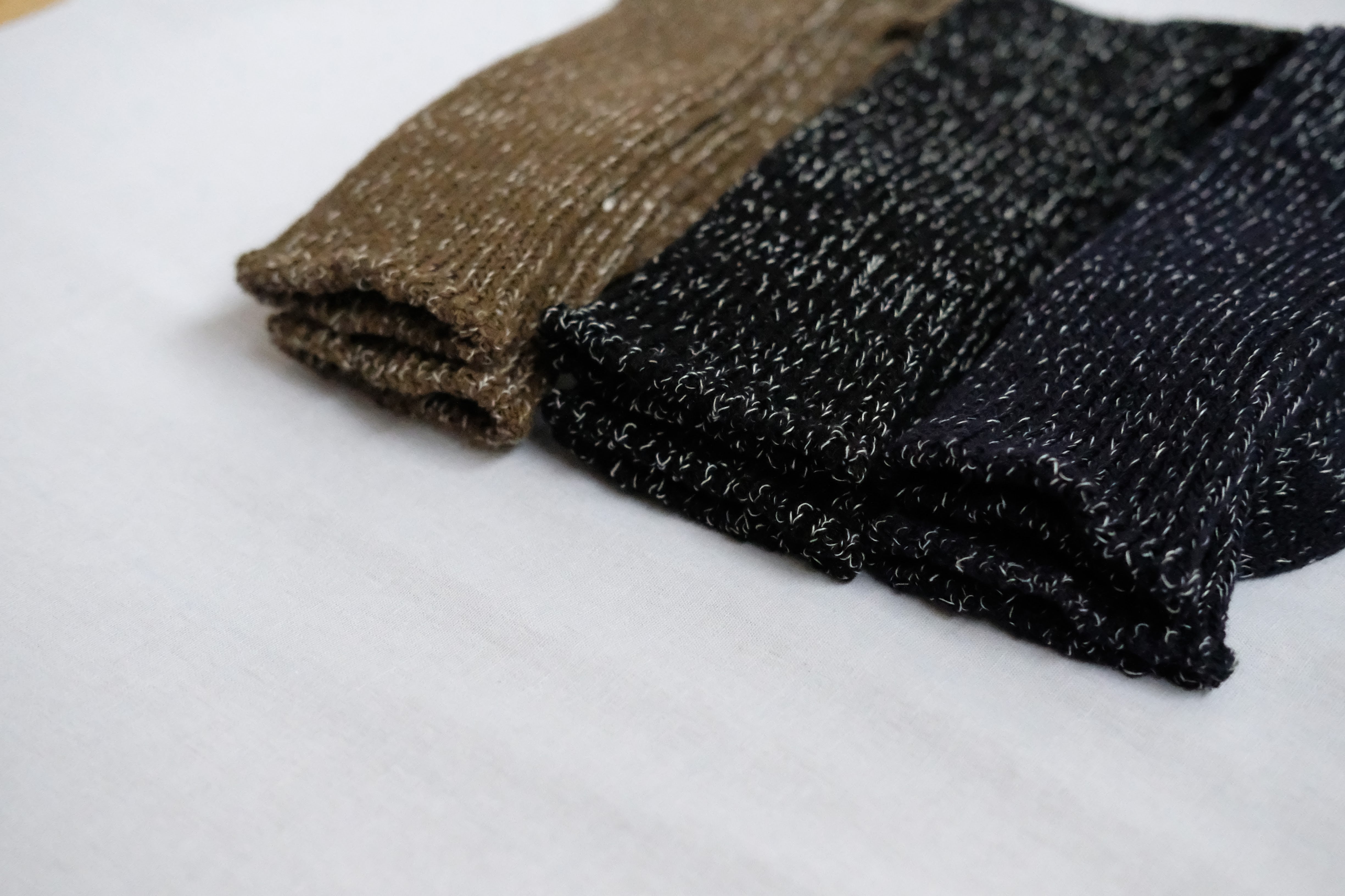 Three pairs of folded knit socks in brown, dark gray, and navy.  The socks have a speckled pattern.