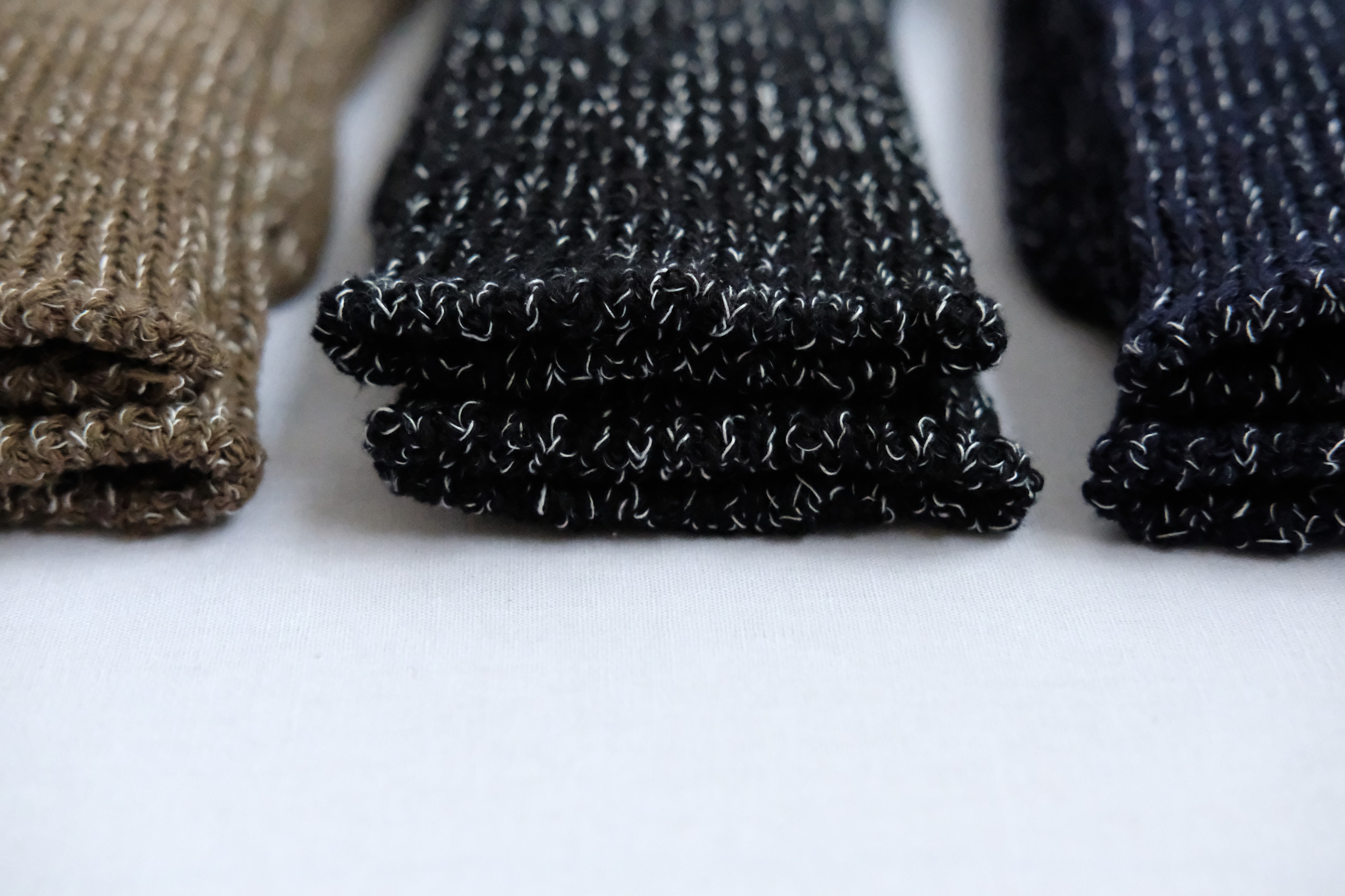 Three pairs of folded knit socks in brown, black with white flecks, and navy.