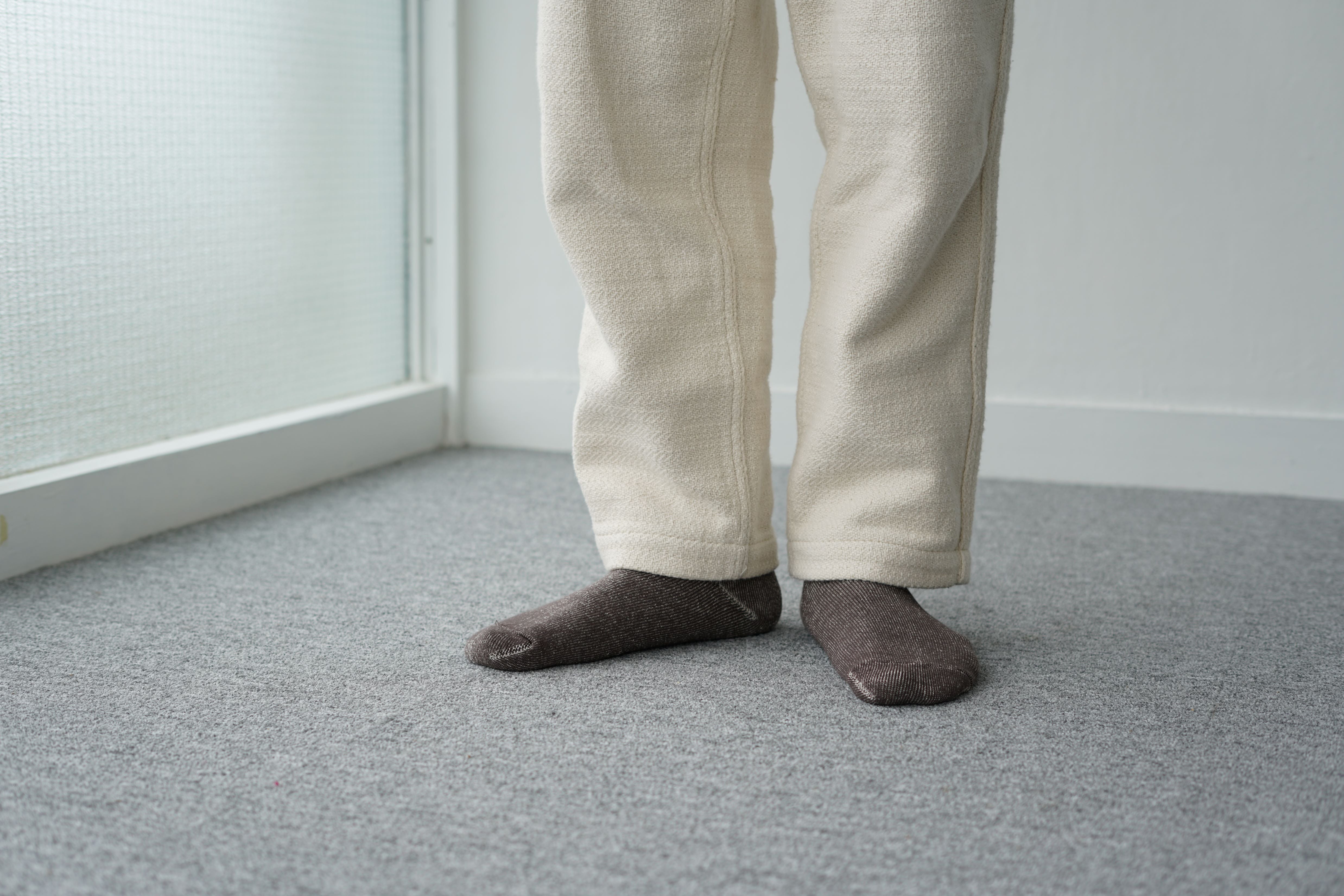 Off-white textured pants and dark gray ribbed socks on a gray carpet.