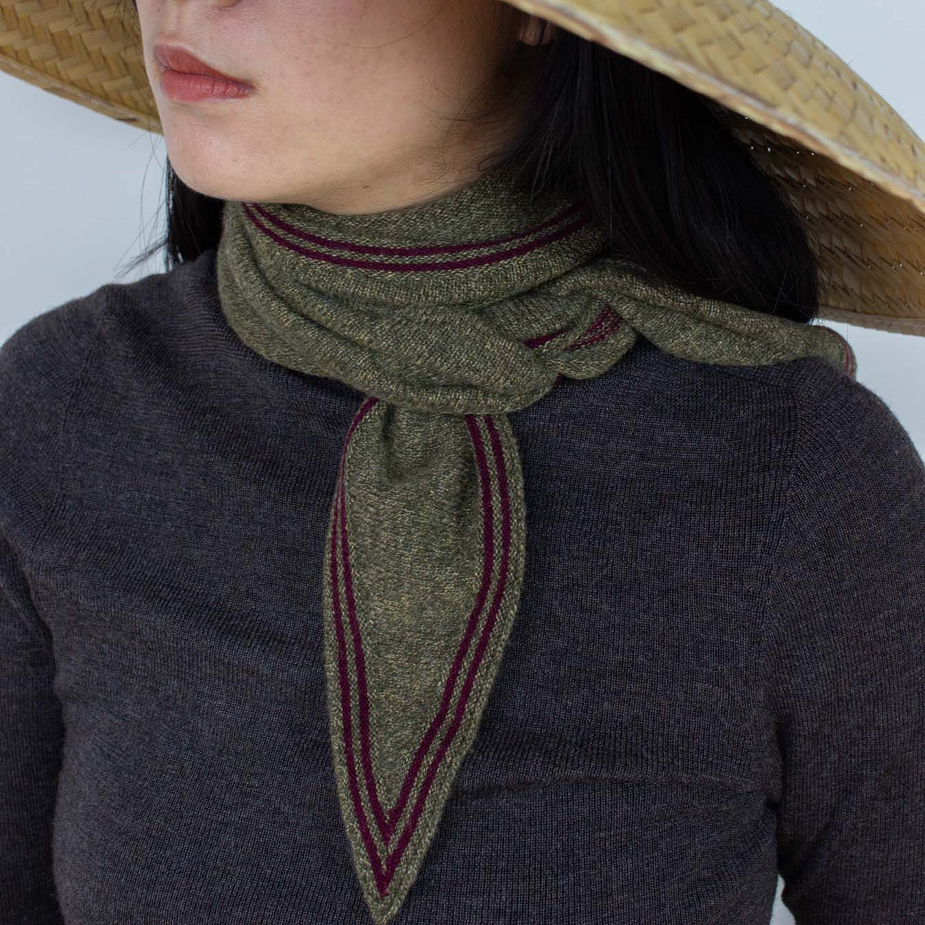 Person wearing a wide-brimmed straw hat and a dark sweater with a green scarf.