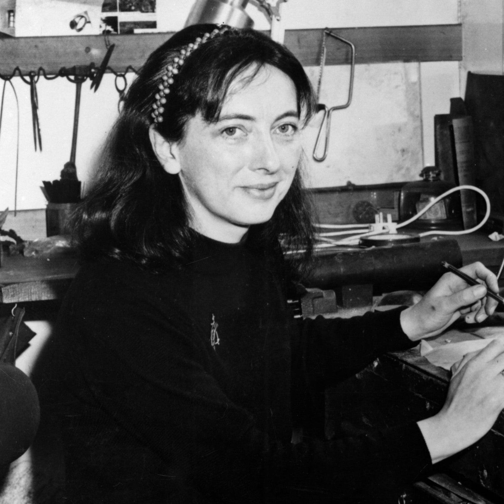 Black and white photo of a woman sitting at a desk with tools and materials.