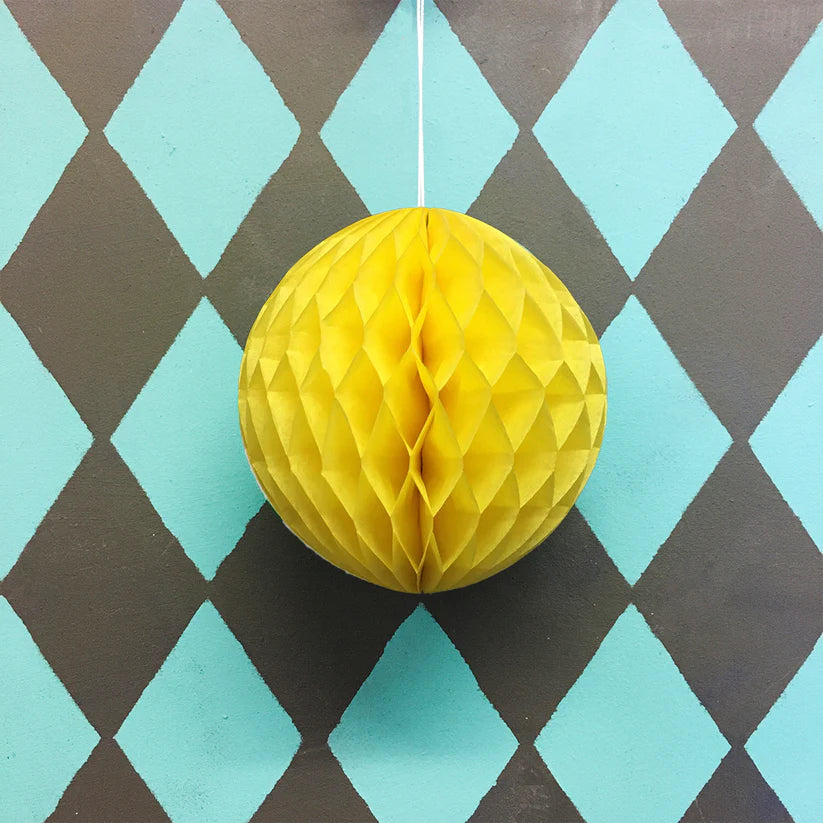 Yellow honeycomb paper ball hanging against a teal and brown diamond pattern background.