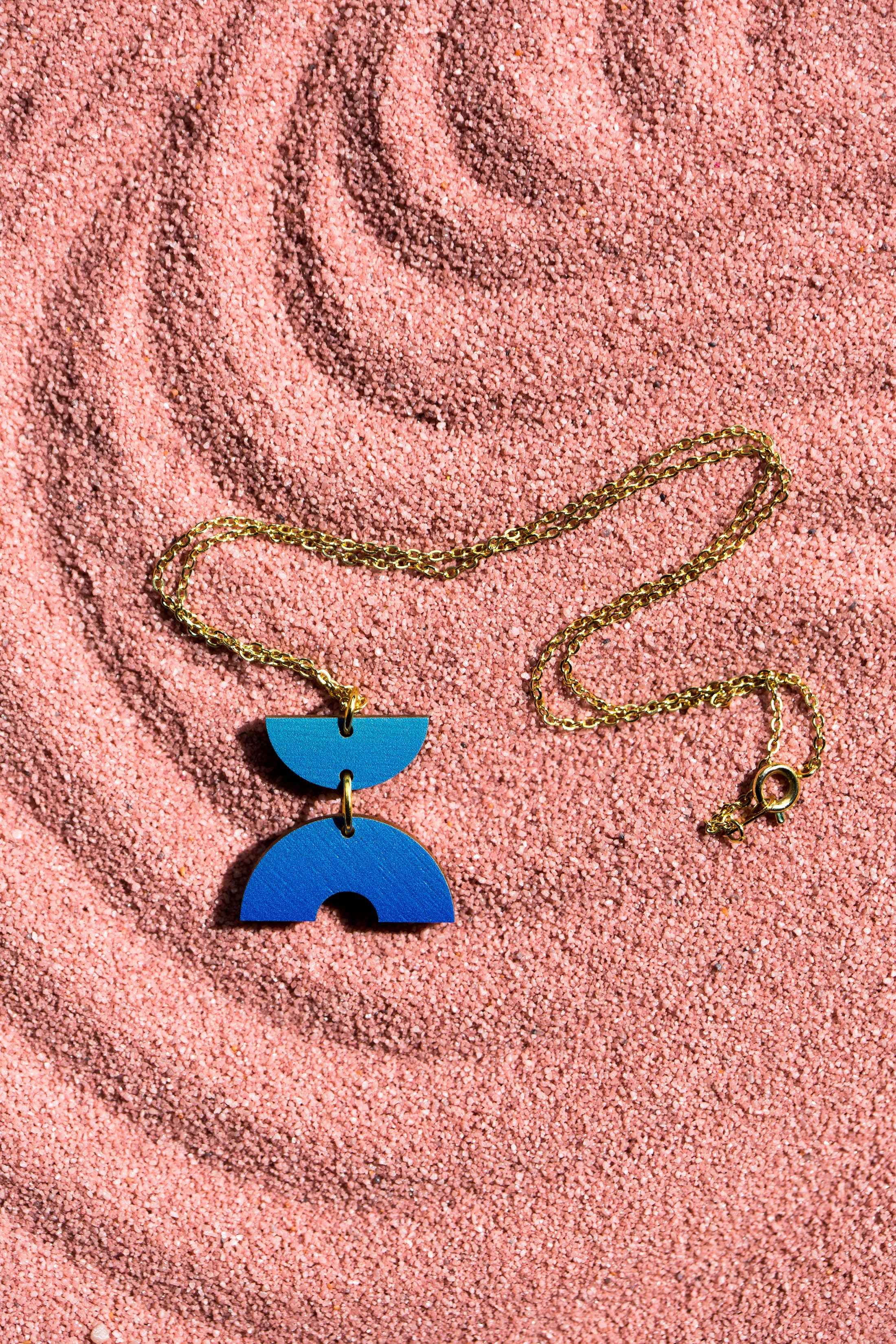 Gold chain necklace with a blue ombre wooden pendant featuring two semi-circle shapes.