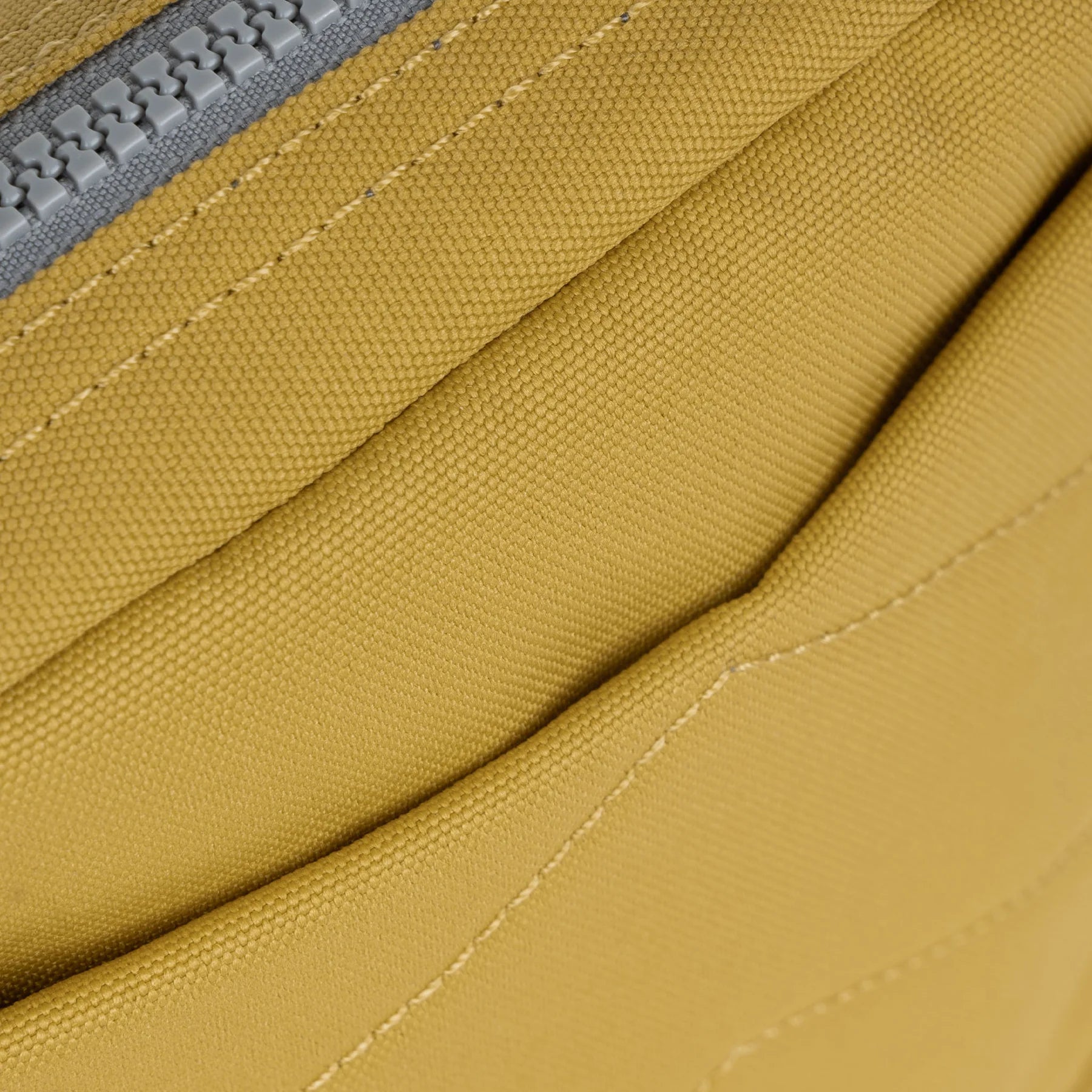 Close-up of mustard yellow canvas fabric with a gray zipper and subtle stitching detail.
