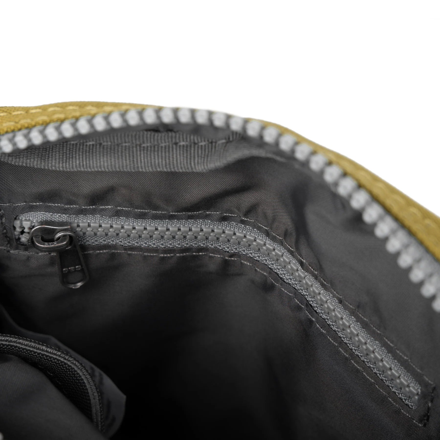Close-up of a mustard-colored bag's interior, showing a grey zippered pocket and dark grey lining.