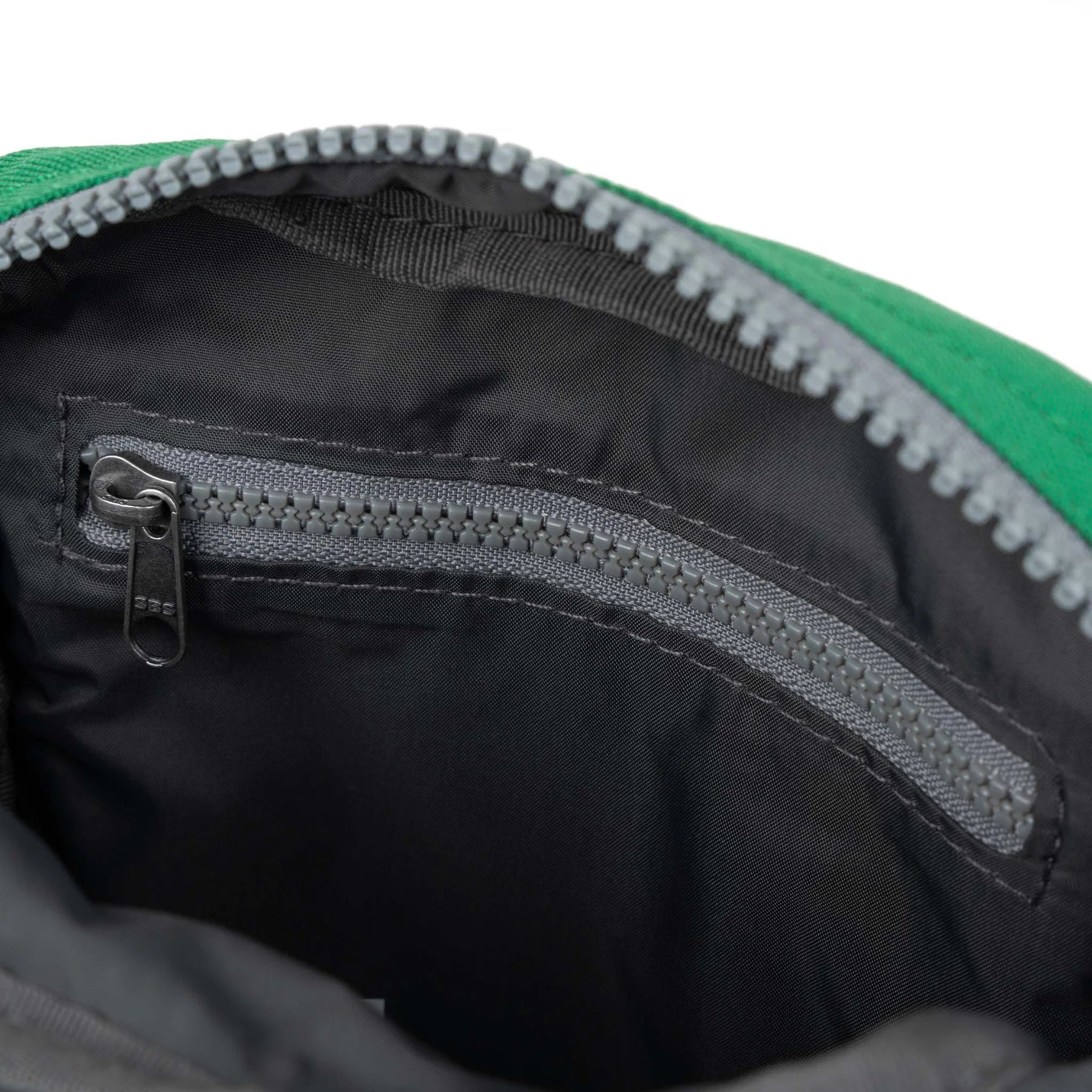 Close-up of a green bag's interior, showcasing a gray zipper and black fabric lining.