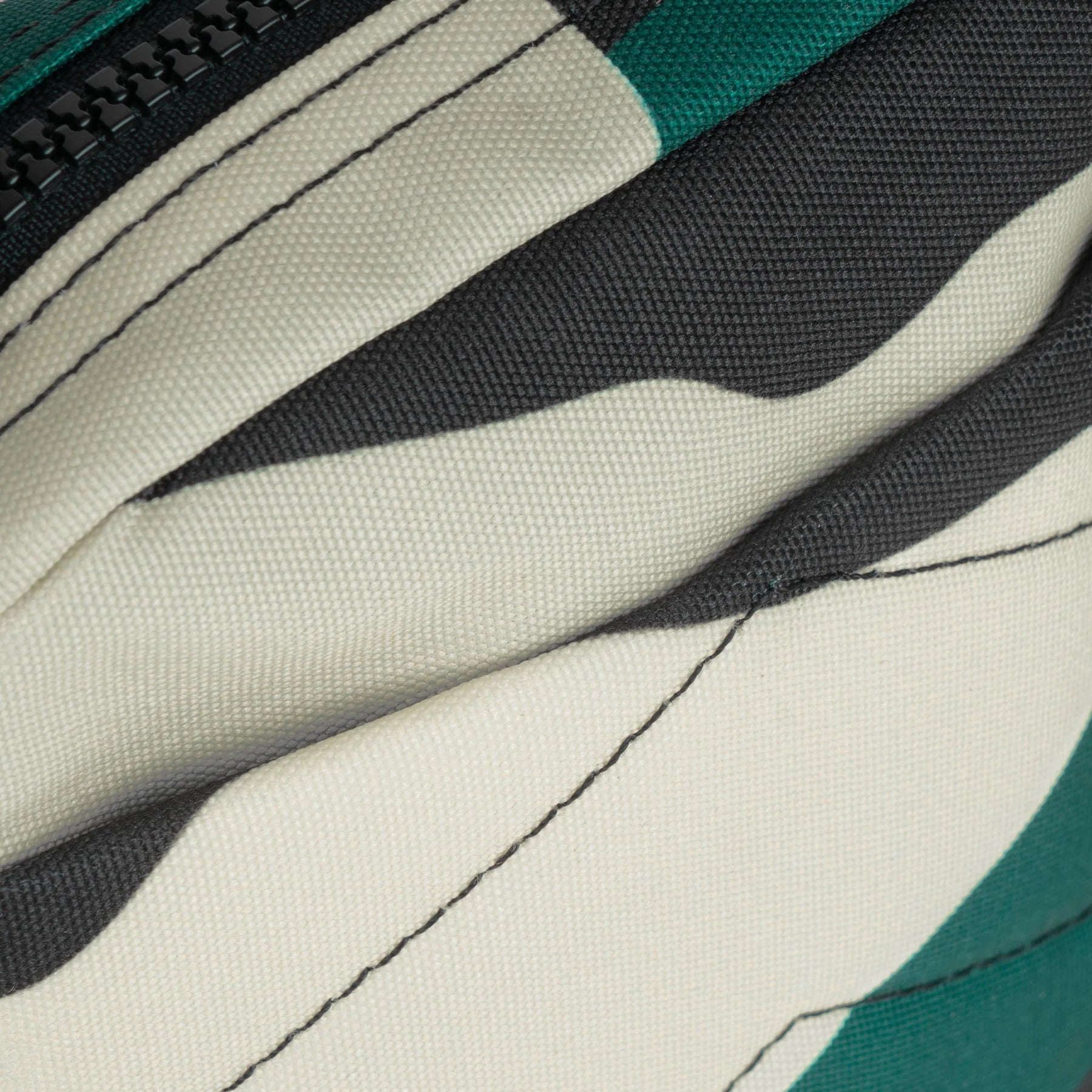 Close-up of a cream, black, and teal canvas bag with a black zipper. The fabric has a textured weave.