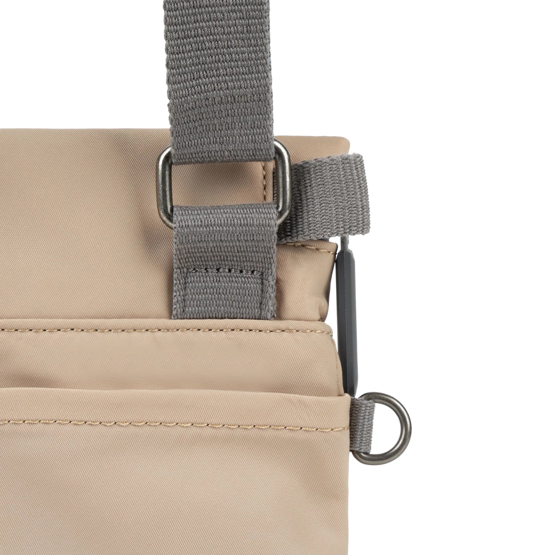 Close-up of ROKA bag showing adjustable gray strap and utility loops on a beige fabric surface.