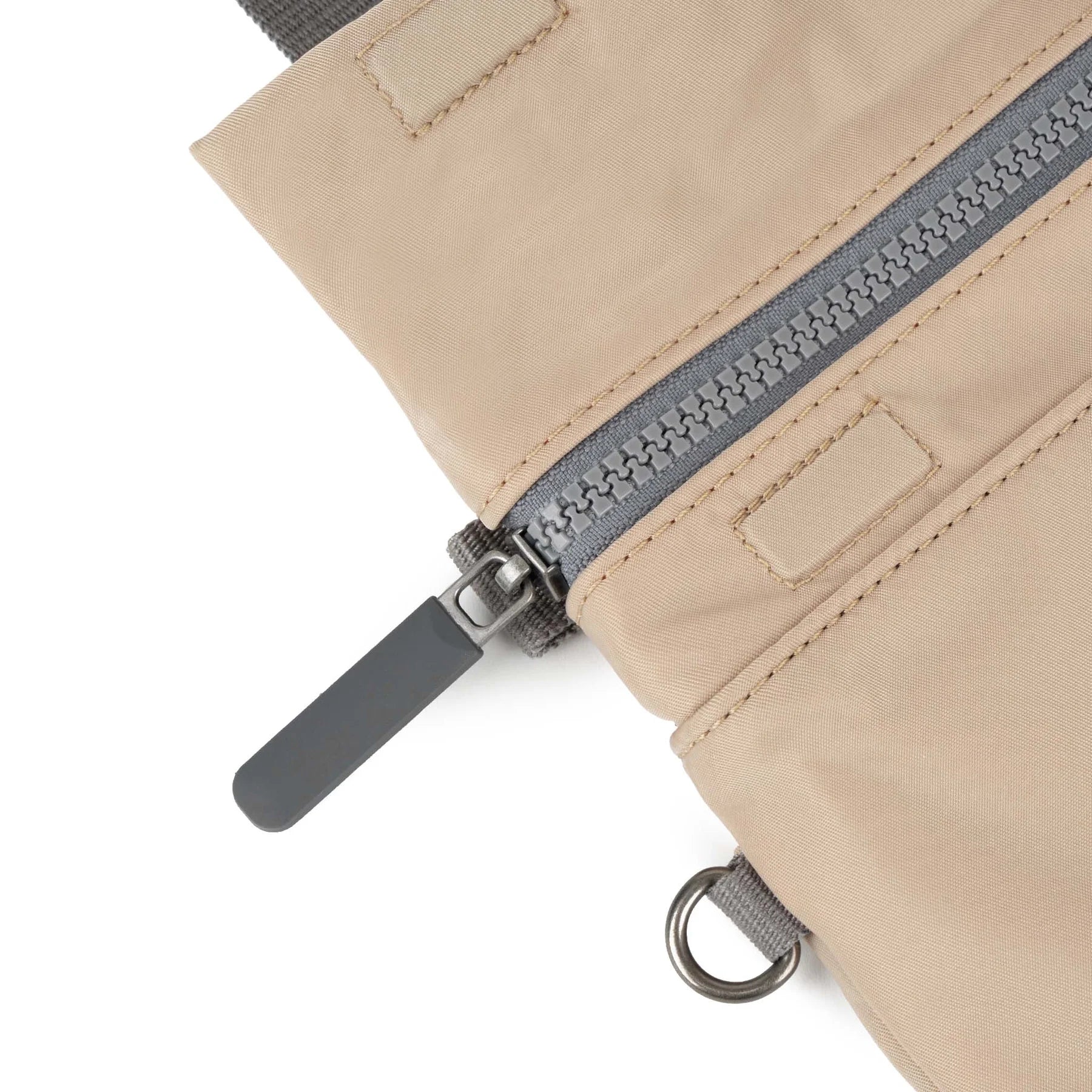 Close-up of a beige ROKA bag with a gray zipper and pull tab, showcasing fabric texture and details.