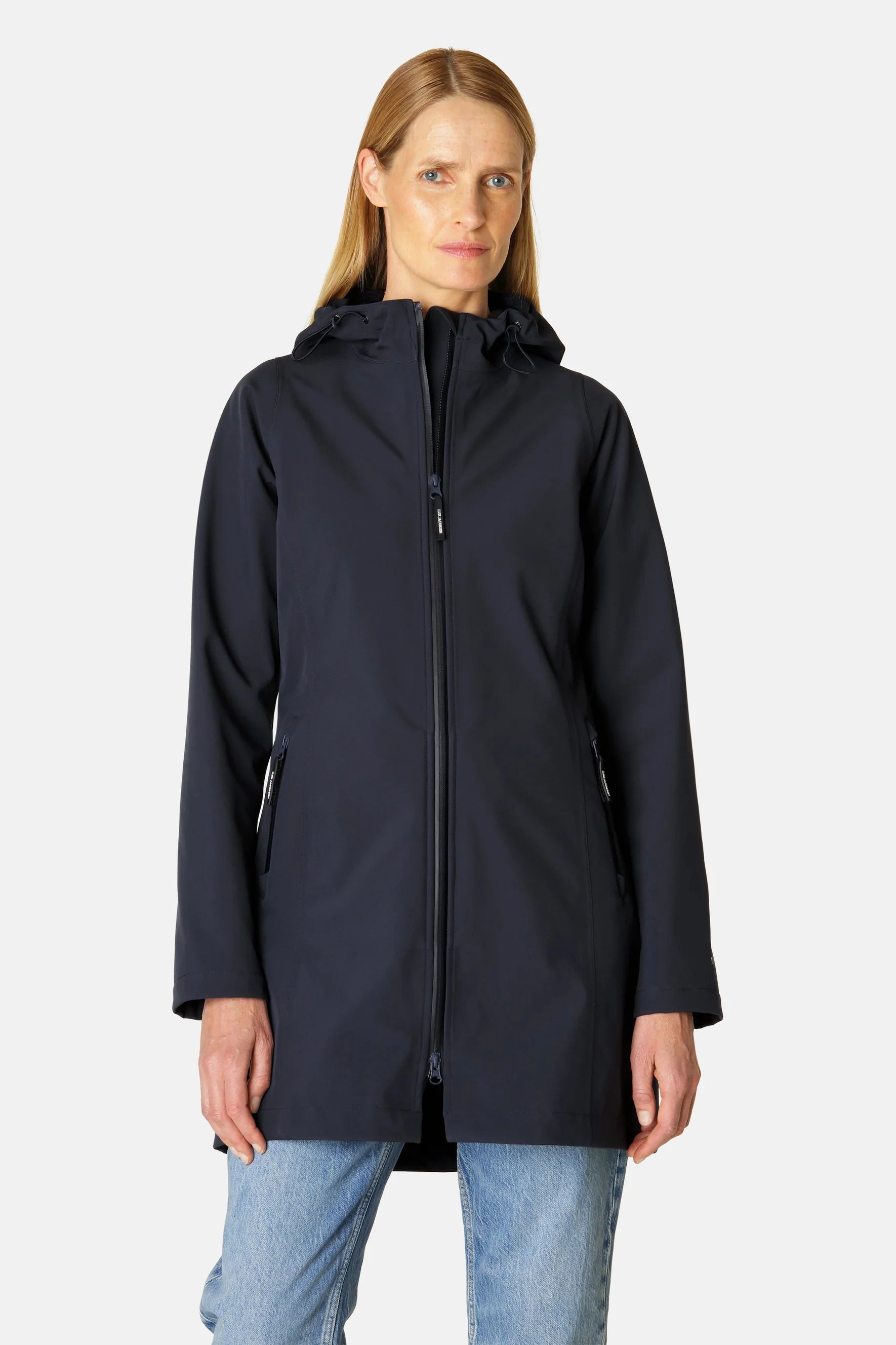 Navy blue women's softshell hooded jacket with zipper closure, pockets, and subtle branding. Model wears light wash jeans.