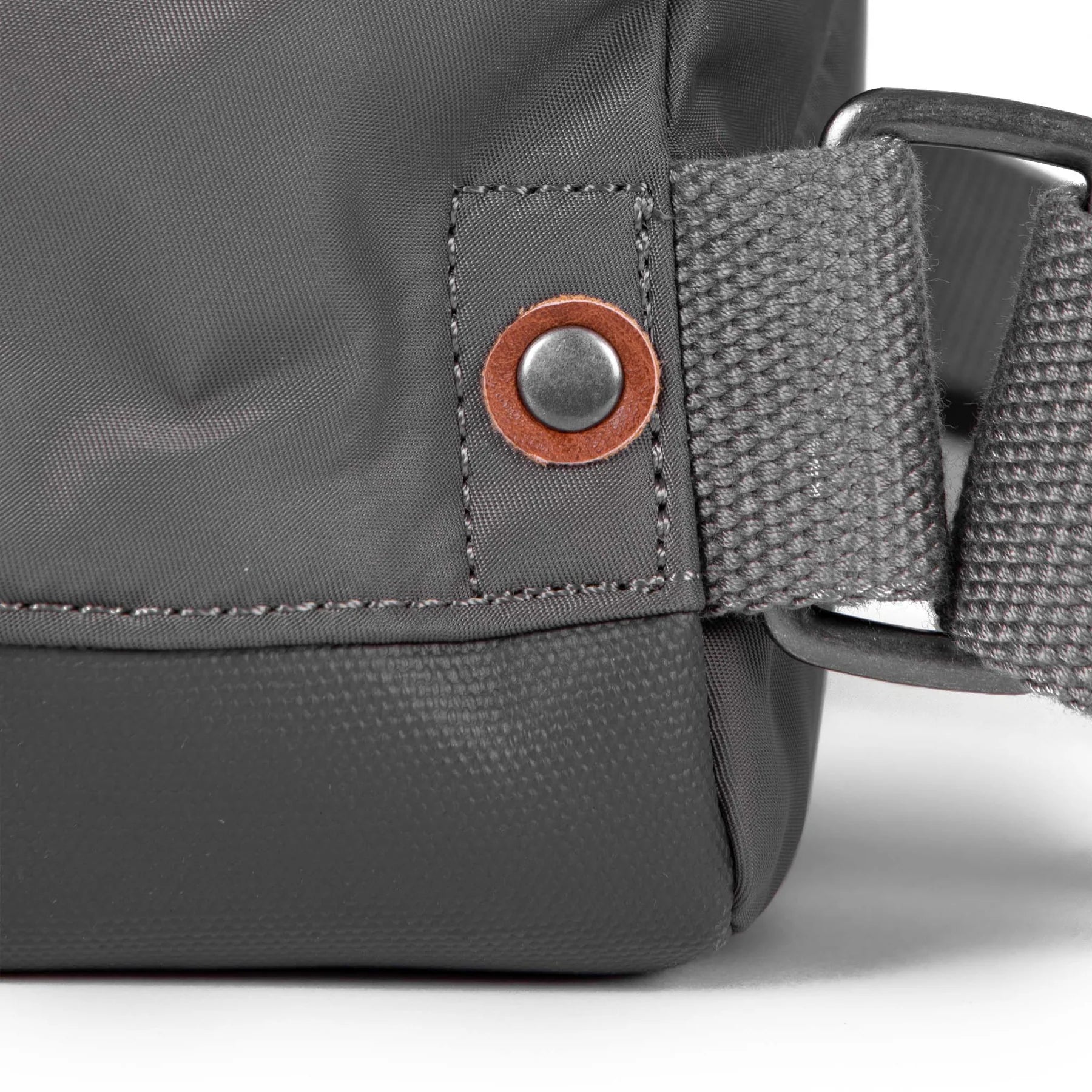 Close-up of a dark gray bag's detail, showing textured fabric, a brown leather accent, and a dark gray strap with a metal