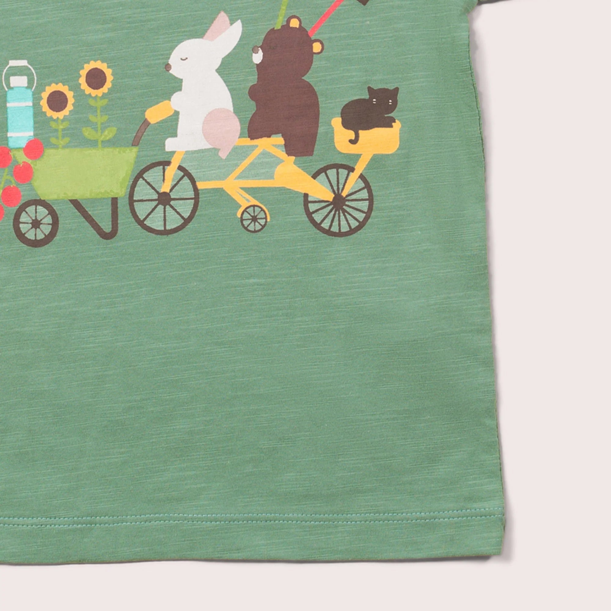 Sage green t-shirt featuring a whimsical illustration of a rabbit and bear riding a tandem bicycle, a cat in a basket, and a