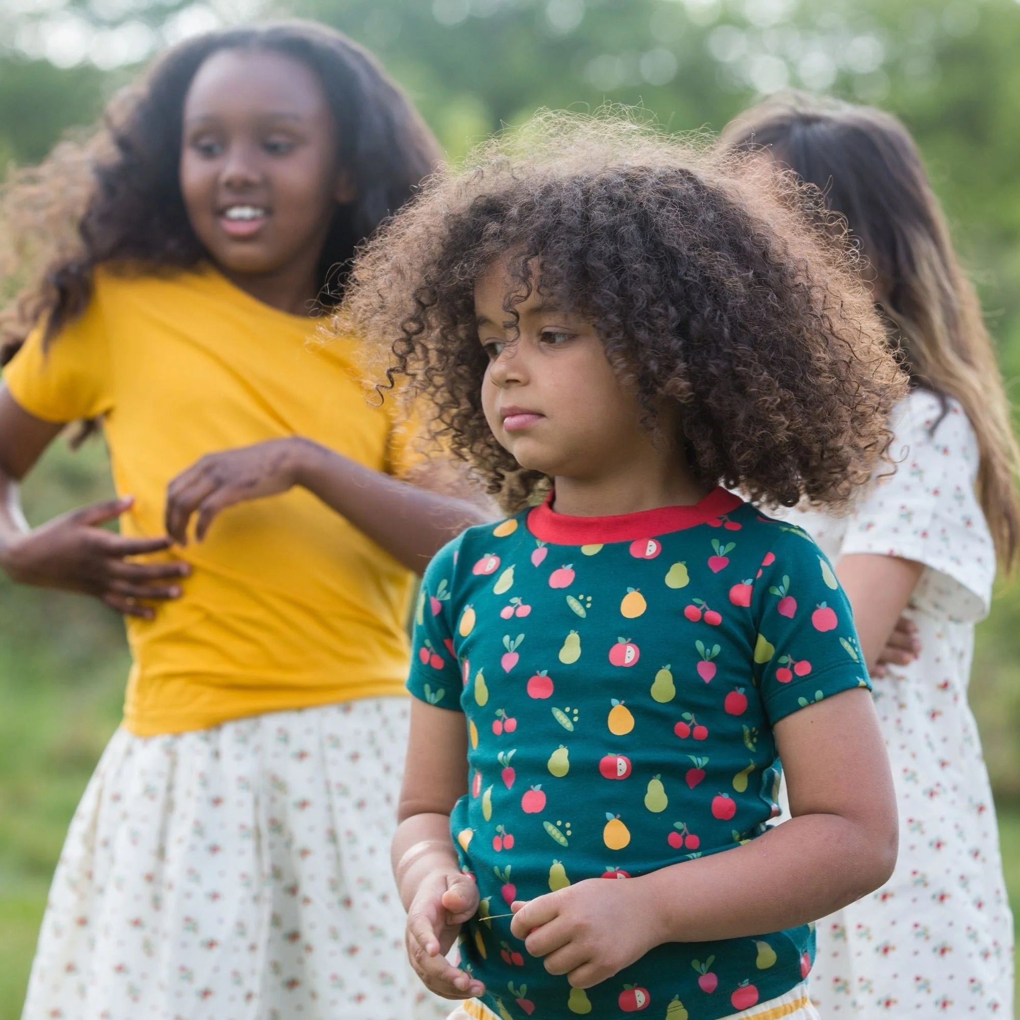 Child wearing a teal short-sleeved shirt with a fruit and vegetable pattern.