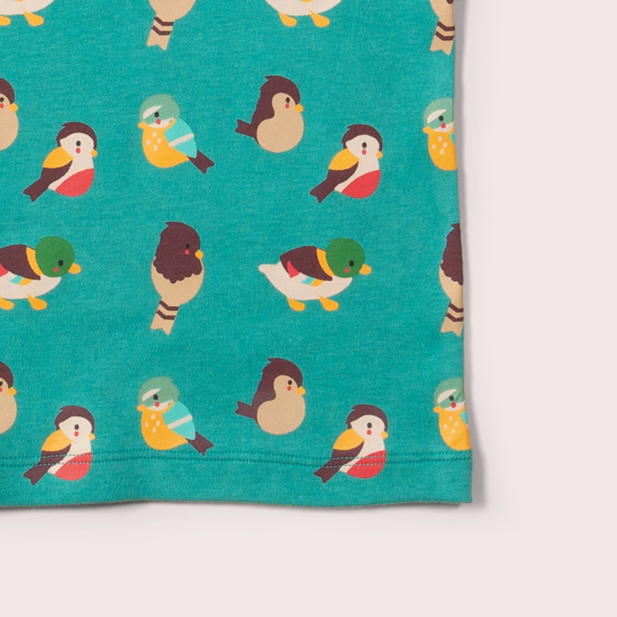 Teal children's shirt with a repeating pattern of colorful illustrated birds and ducks.
