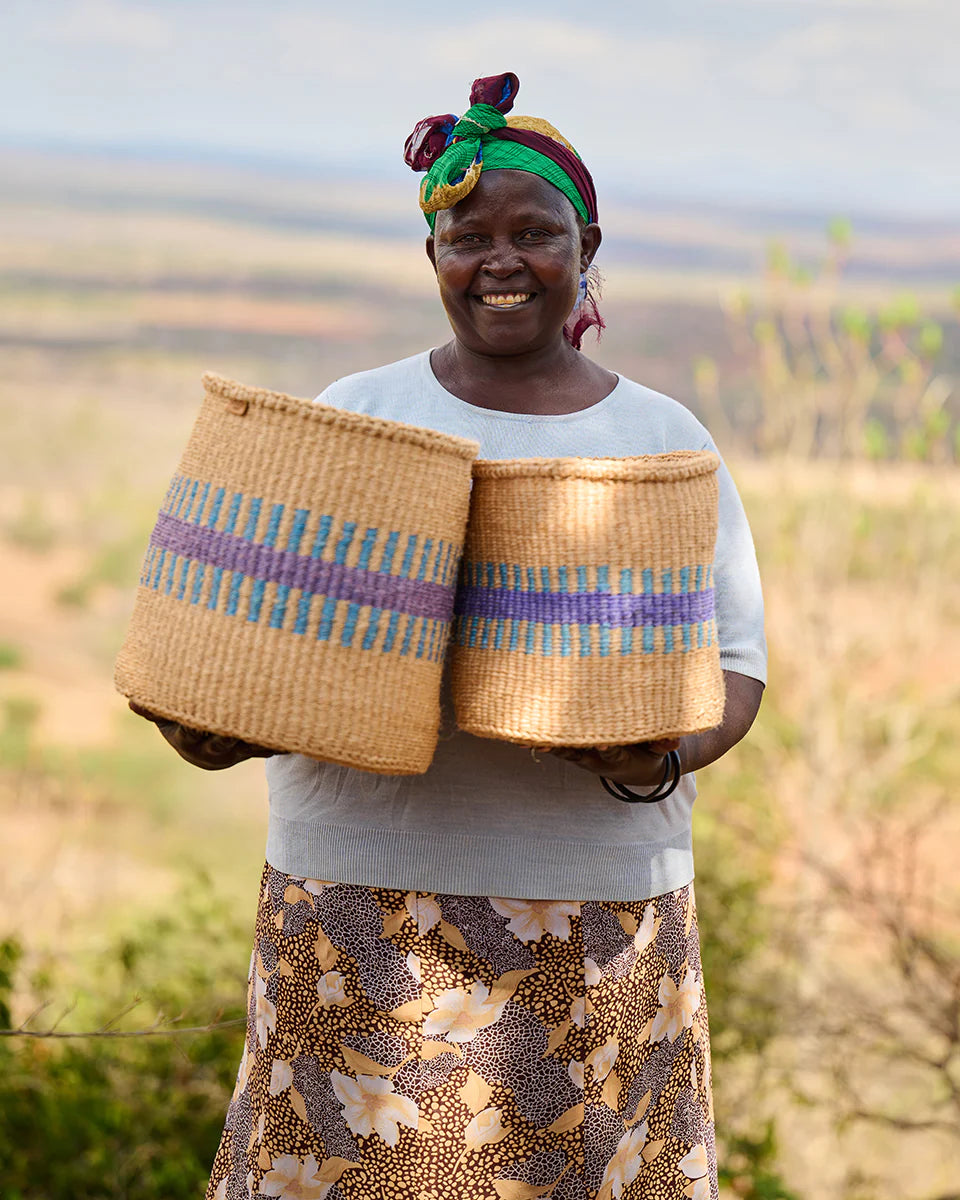 Smiling woman holding two tan woven baskets with blue and purple stripes.