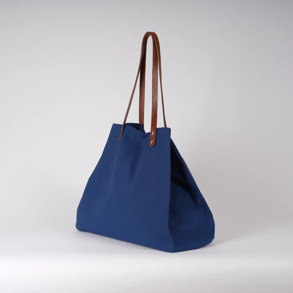 Large cobalt blue tote bag with brown leather handles.