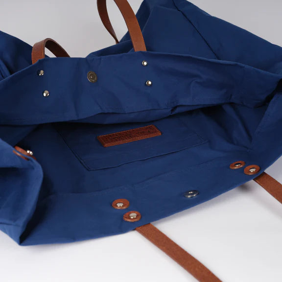 Navy blue canvas tote bag with brown leather straps and metal snap closures.  Interior pocket visible.