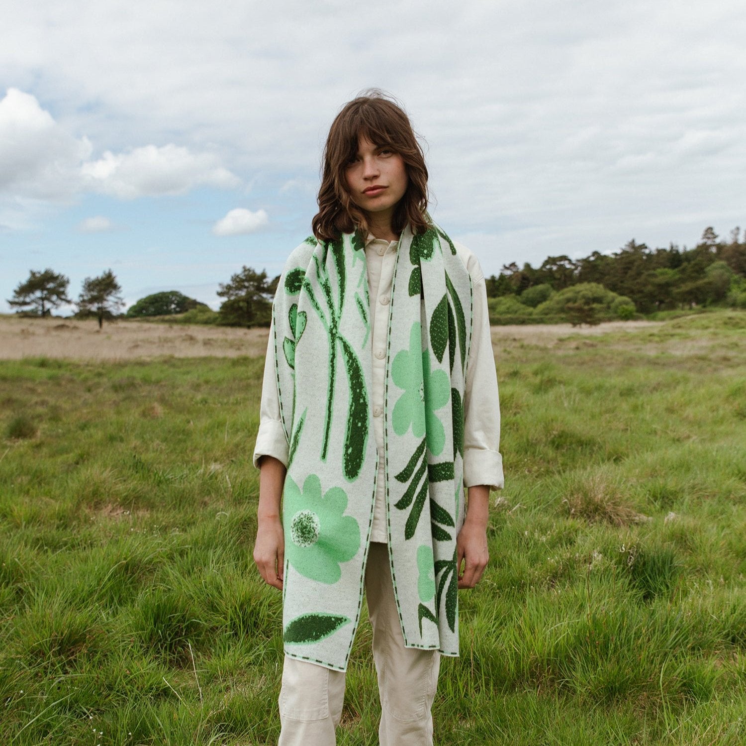 A light beige scarf with a green floral pattern. The design features stylized flowers and leaves.