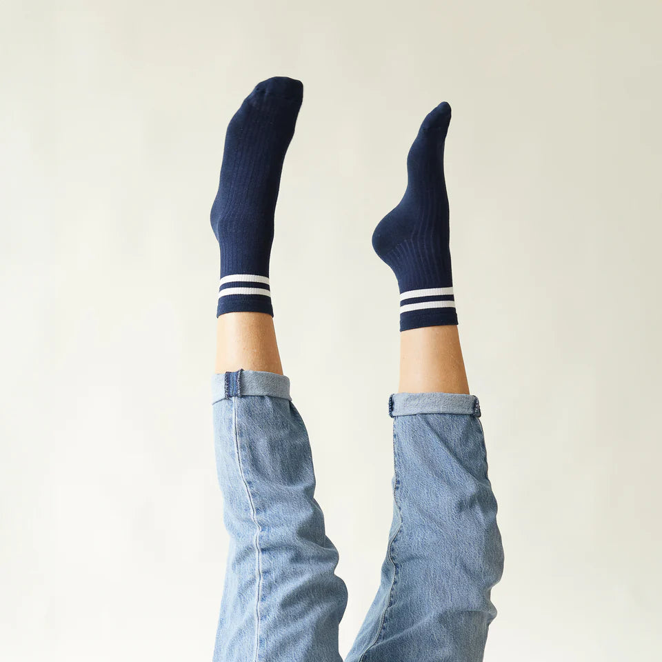 Person wearing navy socks with white stripes and light blue jeans against a plain background