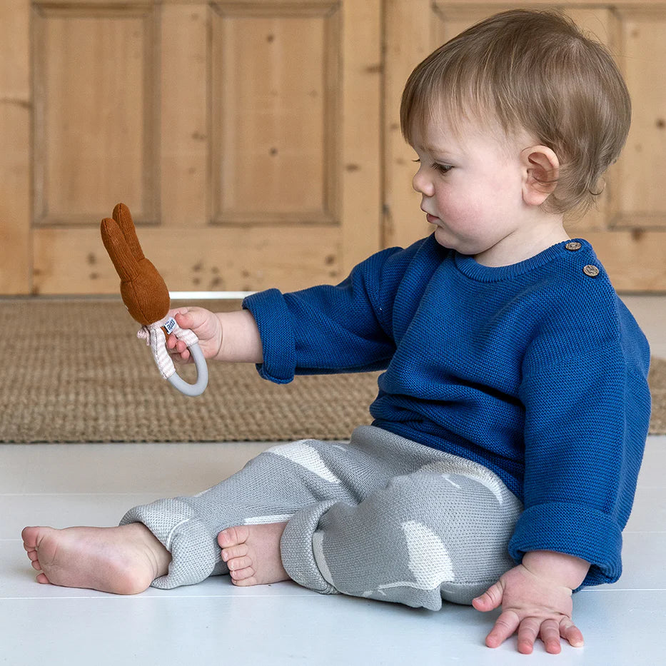 Brown bunny rattle toy with a grey ring handle, held by a baby.