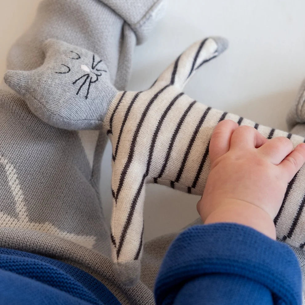 Grey knitted cat toy with a striped body, held by a baby's hand.