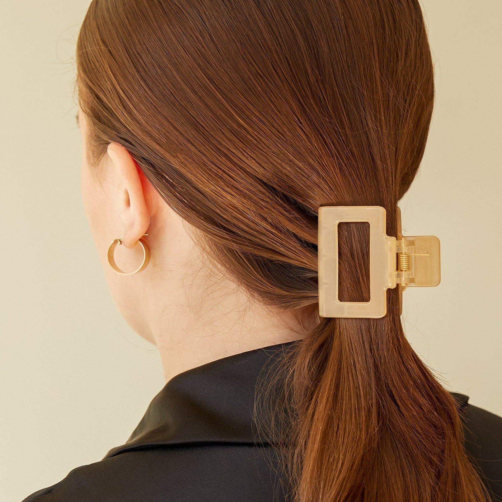 Gold rectangular hair claw clip holding a low ponytail. The clip is translucent with a gold frame.