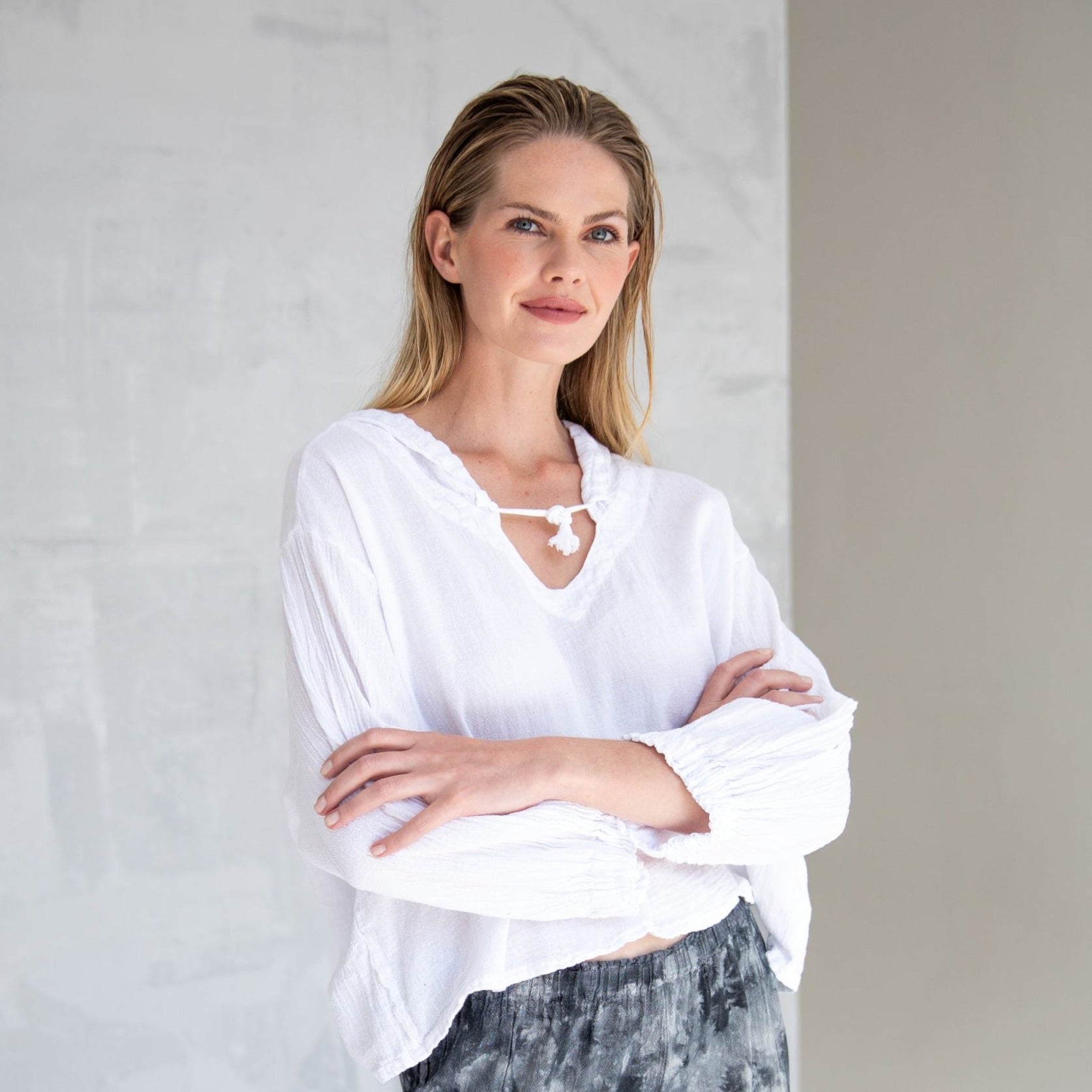 White cotton gauze tunic top with drawstring neckline and gathered sleeves.  Model is wearing it with arms crossed.