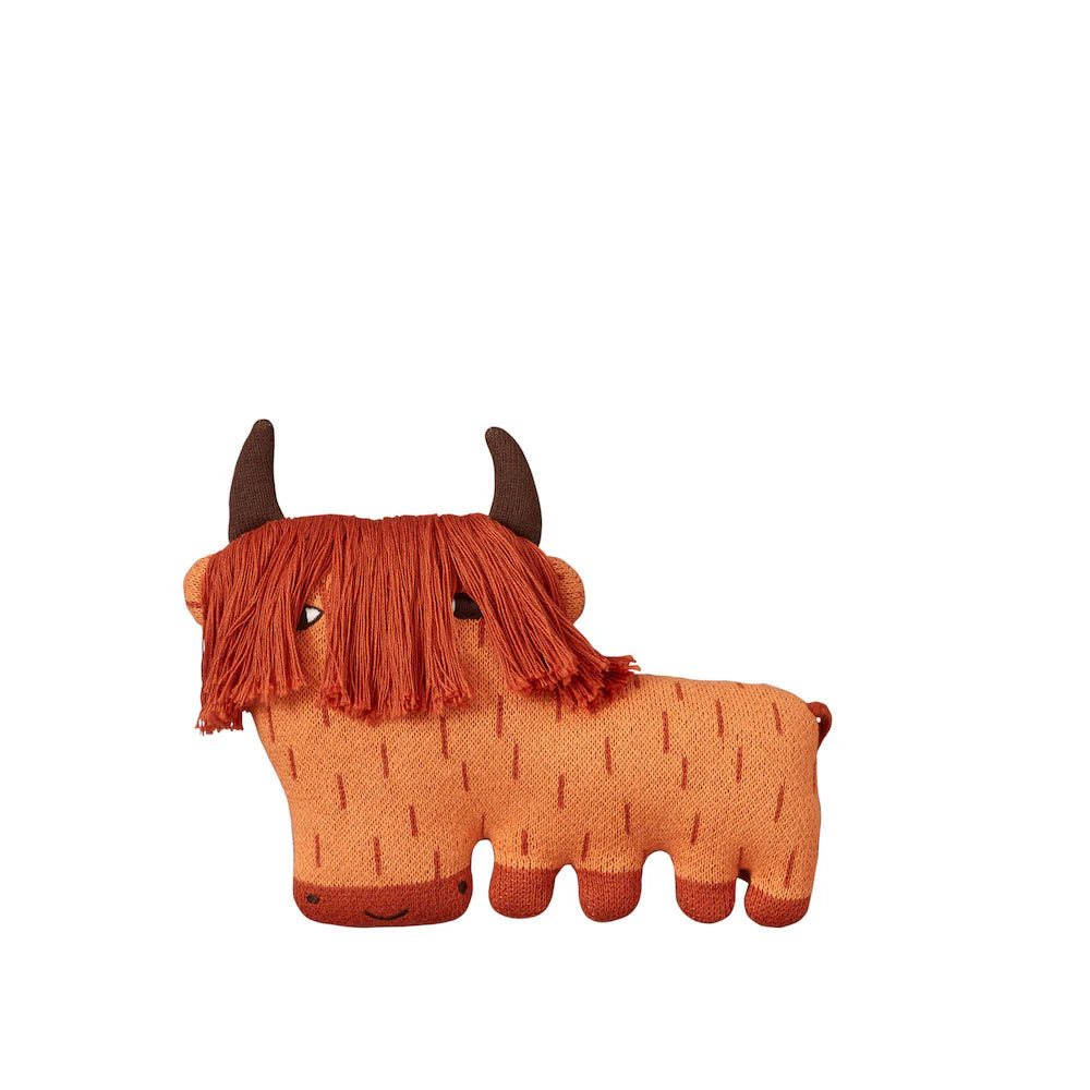 A plush toy by Donna Wilson, featuring brown horns and orange body with fringed orange hair and black eyes.