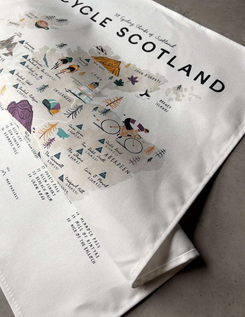 Off-white cotton tea towel featuring a map of Scotland highlighting 30 cycling climbs; illustrated with cyclists and route