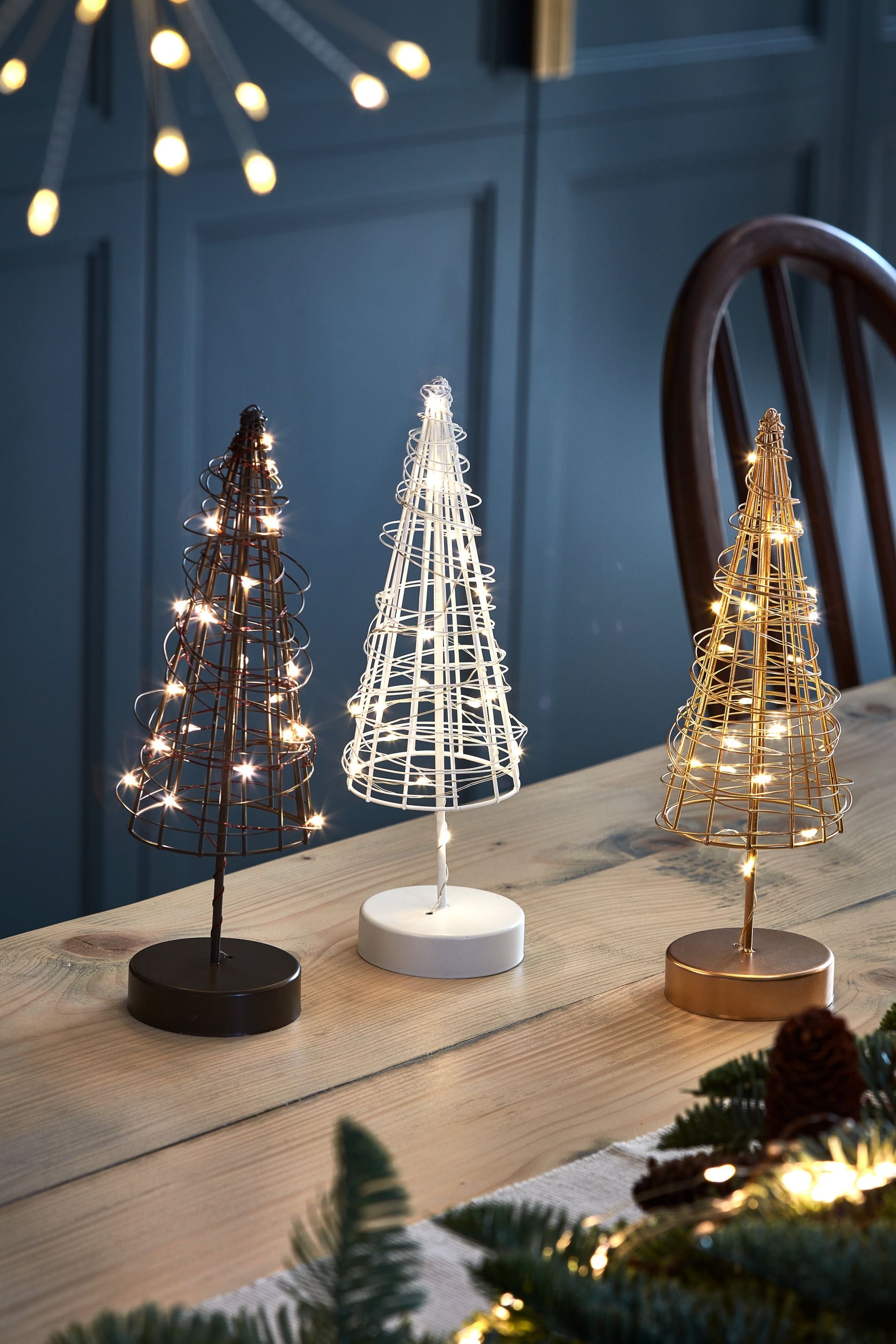 Three illuminated wire Christmas trees in gold, white, and dark brown metal.