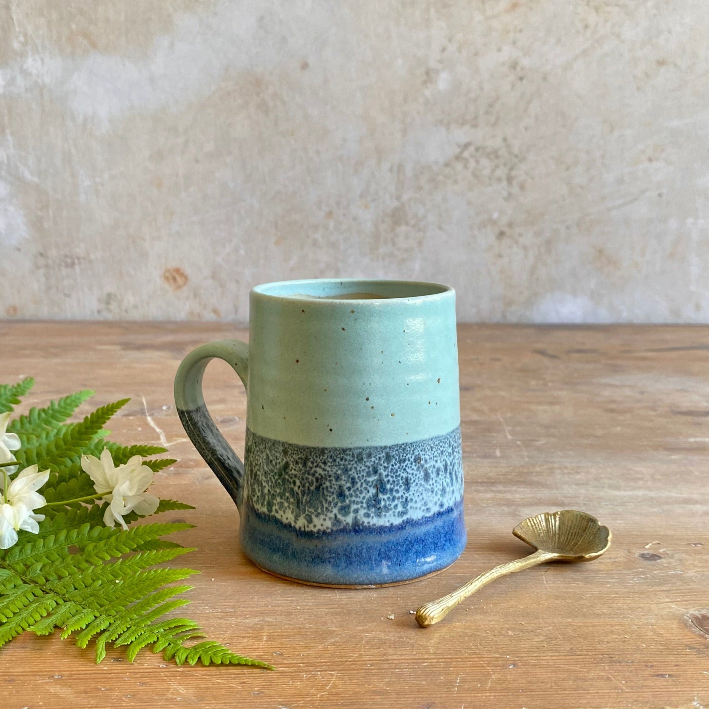 Hand-thrown stoneware mug with a light teal top and a darker blue speckled bottom.