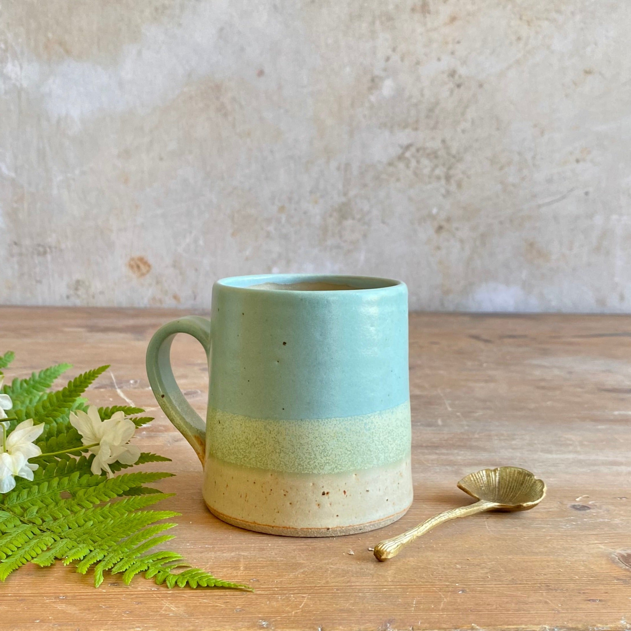 Hand-thrown stoneware mug with a light teal, pale green, and off-white speckled glaze.
