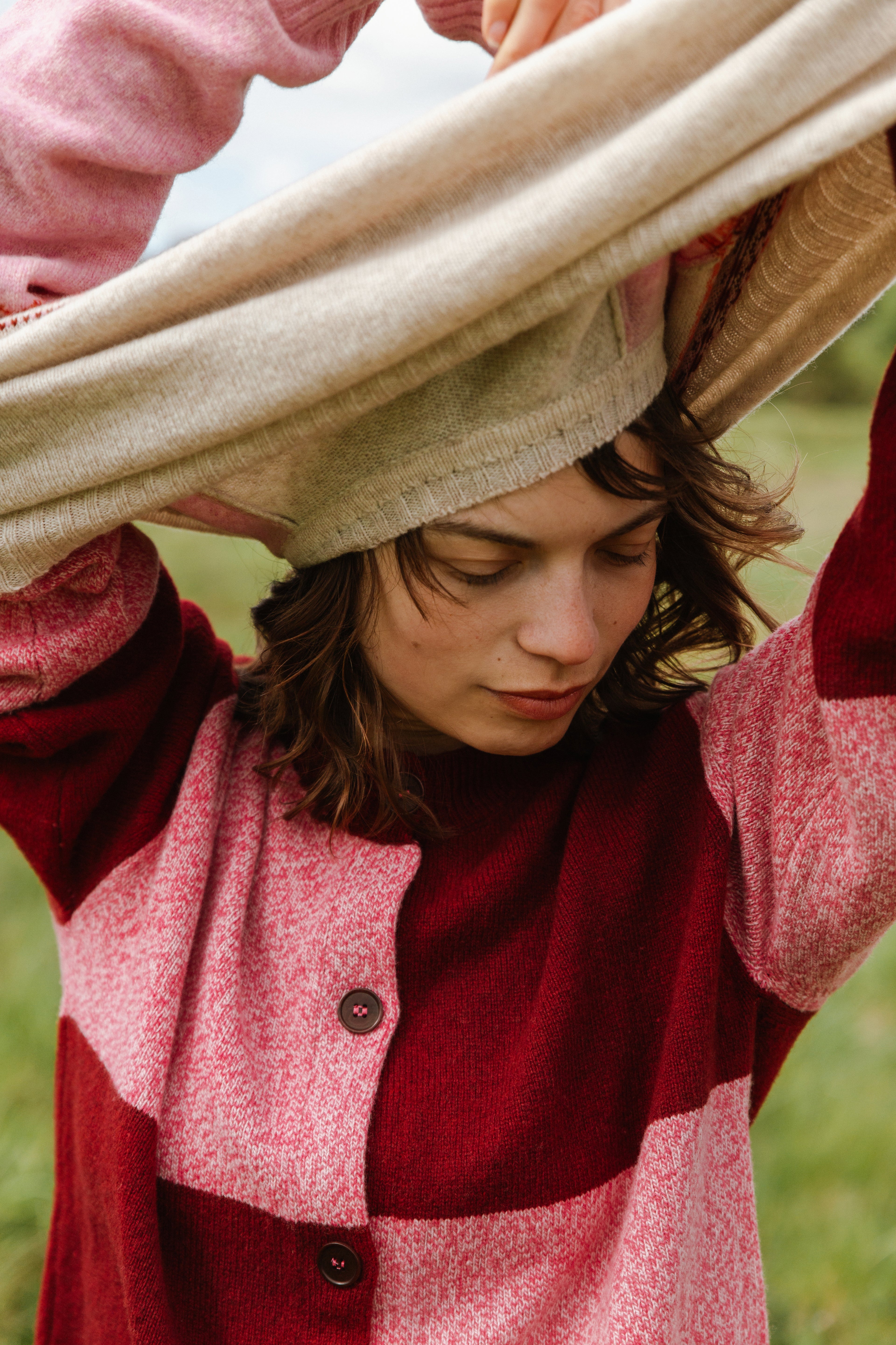 Red and pink color-blocked wool cardigan with wooden buttons, being modeled by a person holding a beige knitted shawl over