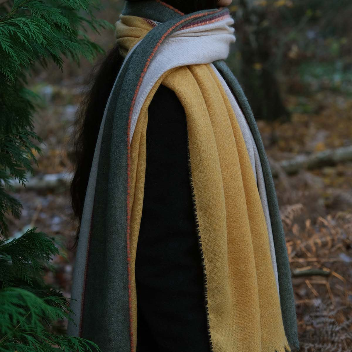 Person wearing a black hat and a colorful scarf in a forest setting