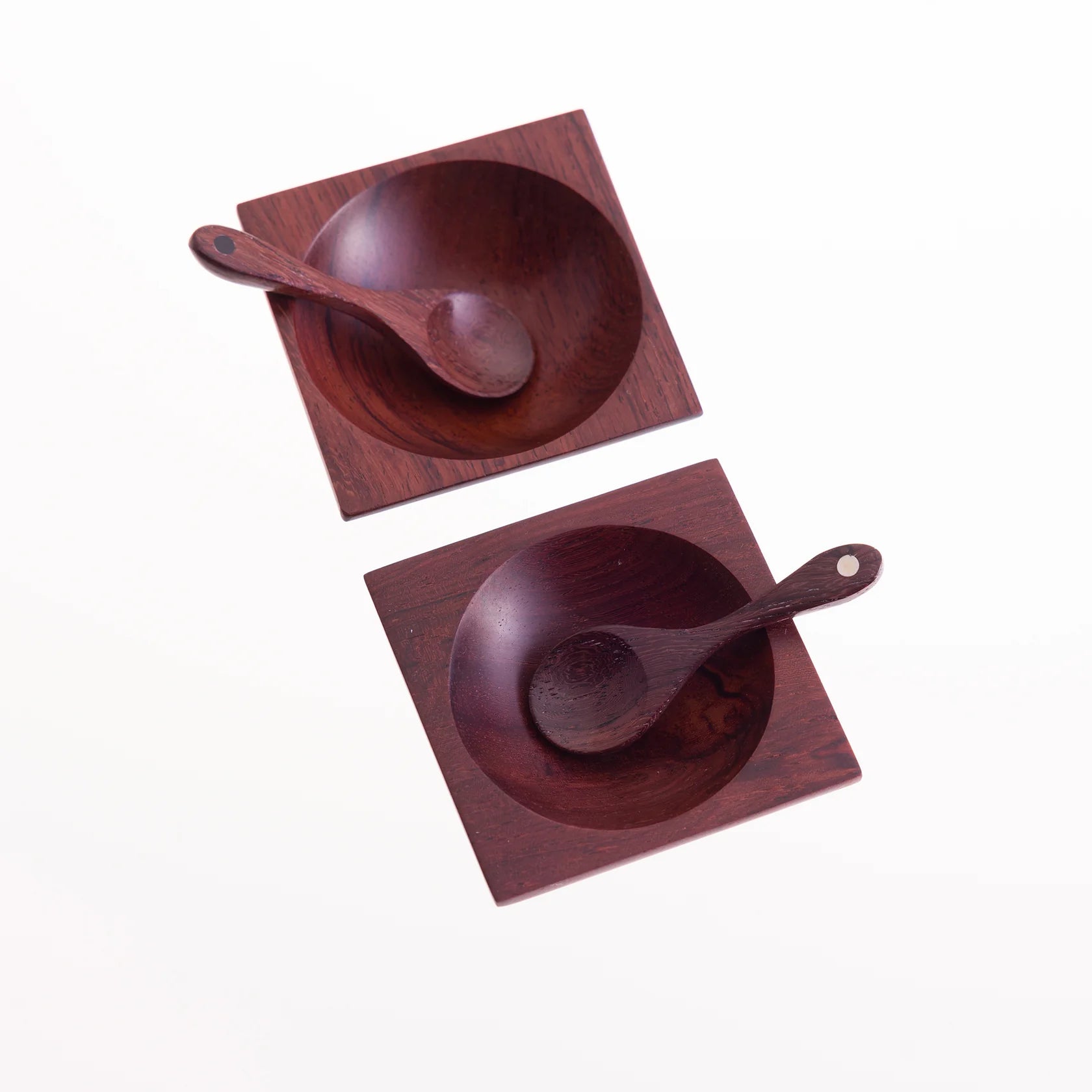 Two dark-red square wooden bowls, each containing a small wooden spoon.