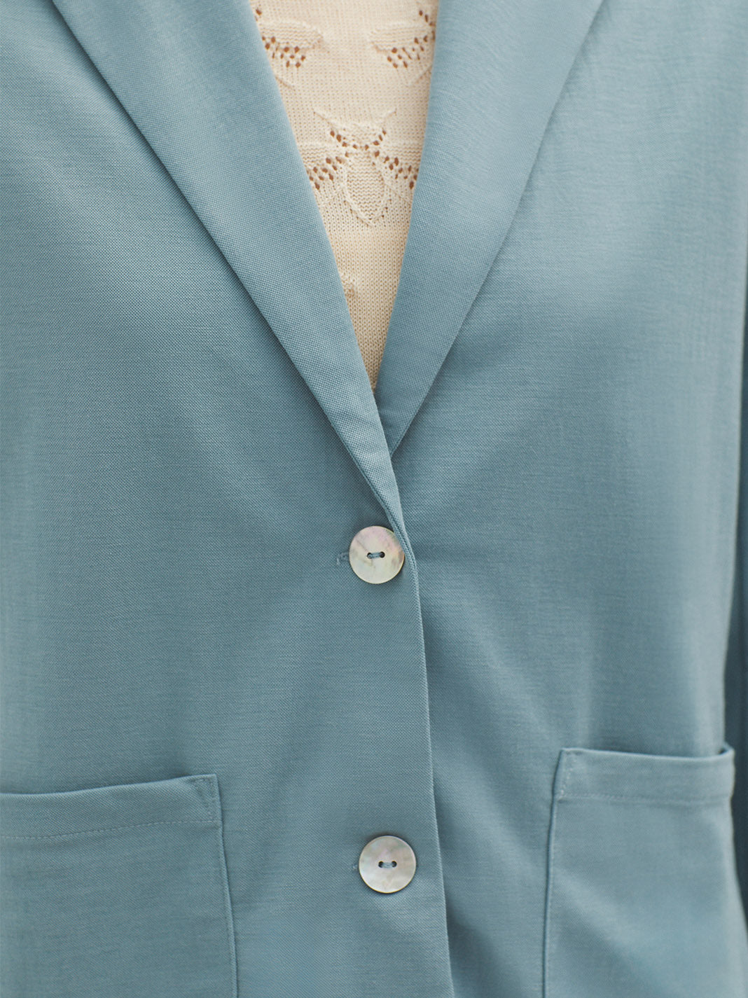 Dusty blue blazer with notched lapels and shell buttons.  Patch pockets are visible at the bottom.