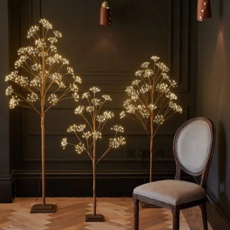 Decorative LED trees in a room with a chair and wall lights.