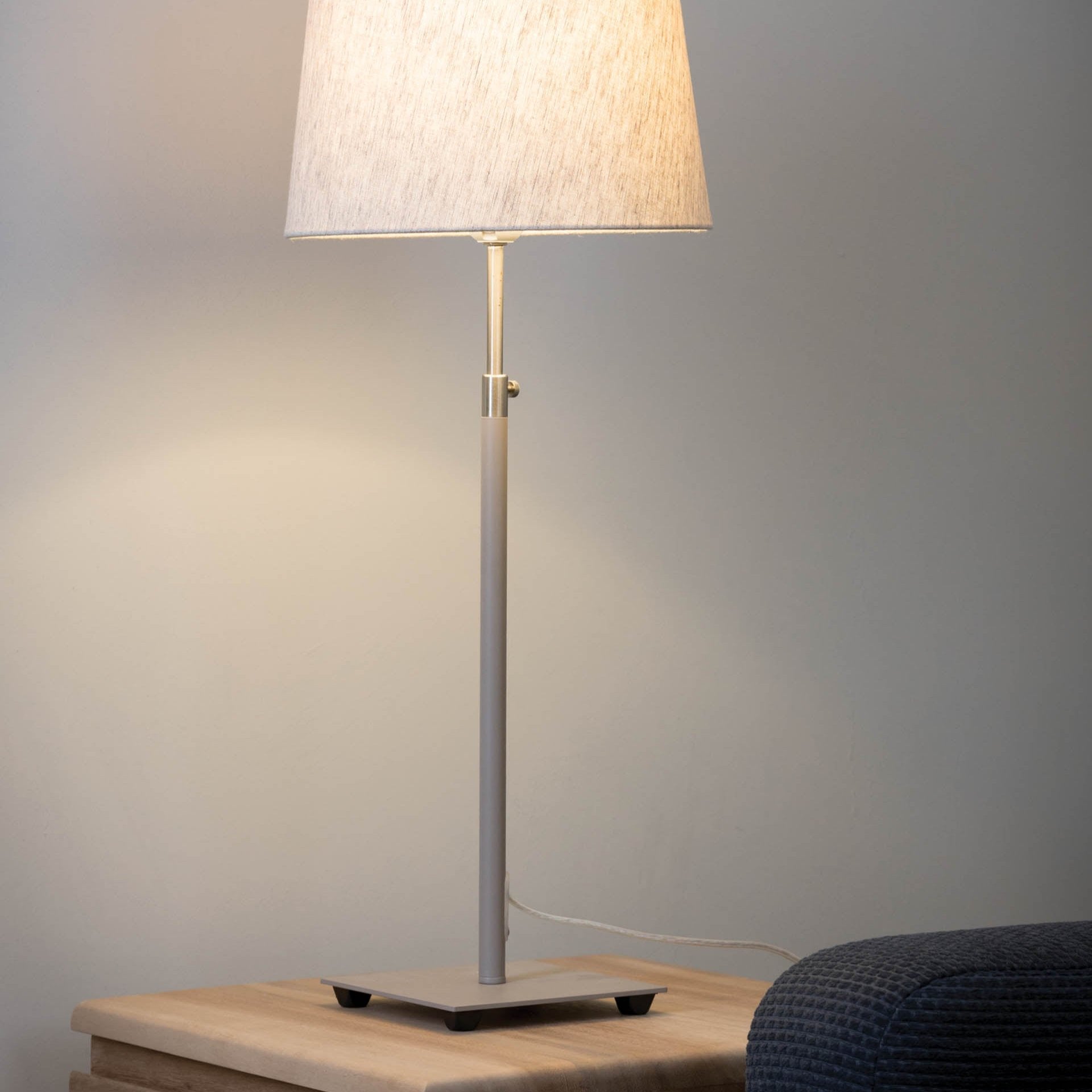 Modern table lamp with a light beige fabric shade and a slender, light grey metal base.