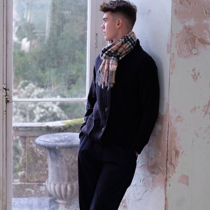 Man wearing a dark cardigan, dark trousers, and a beige and black checked scarf.