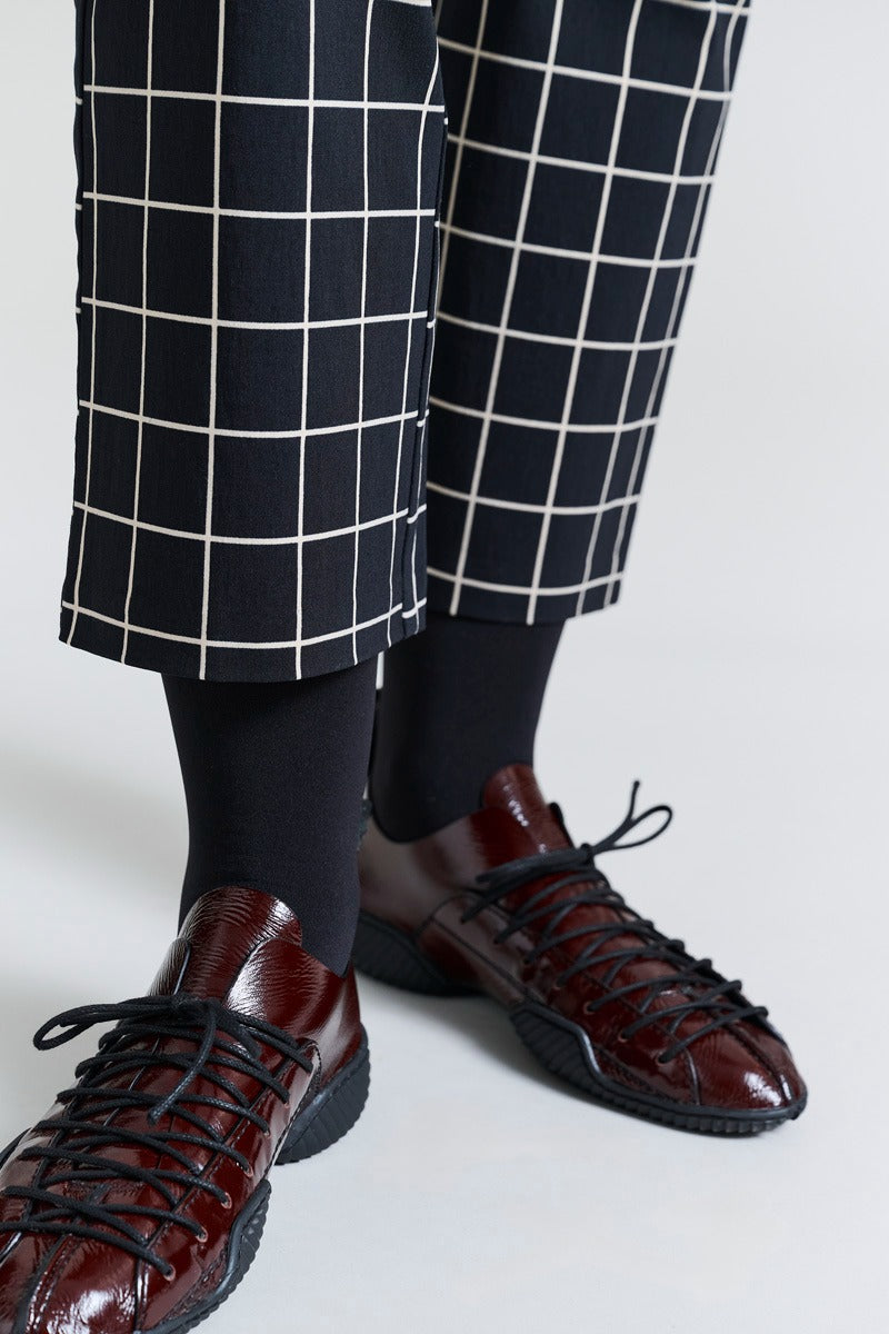 Brown leather shoes with black laces worn with navy checkered pants on a white background