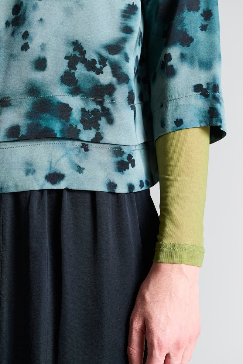 Person wearing a tie-dye shirt with blue and black patterns, a green sleeve, and a gray skirt.