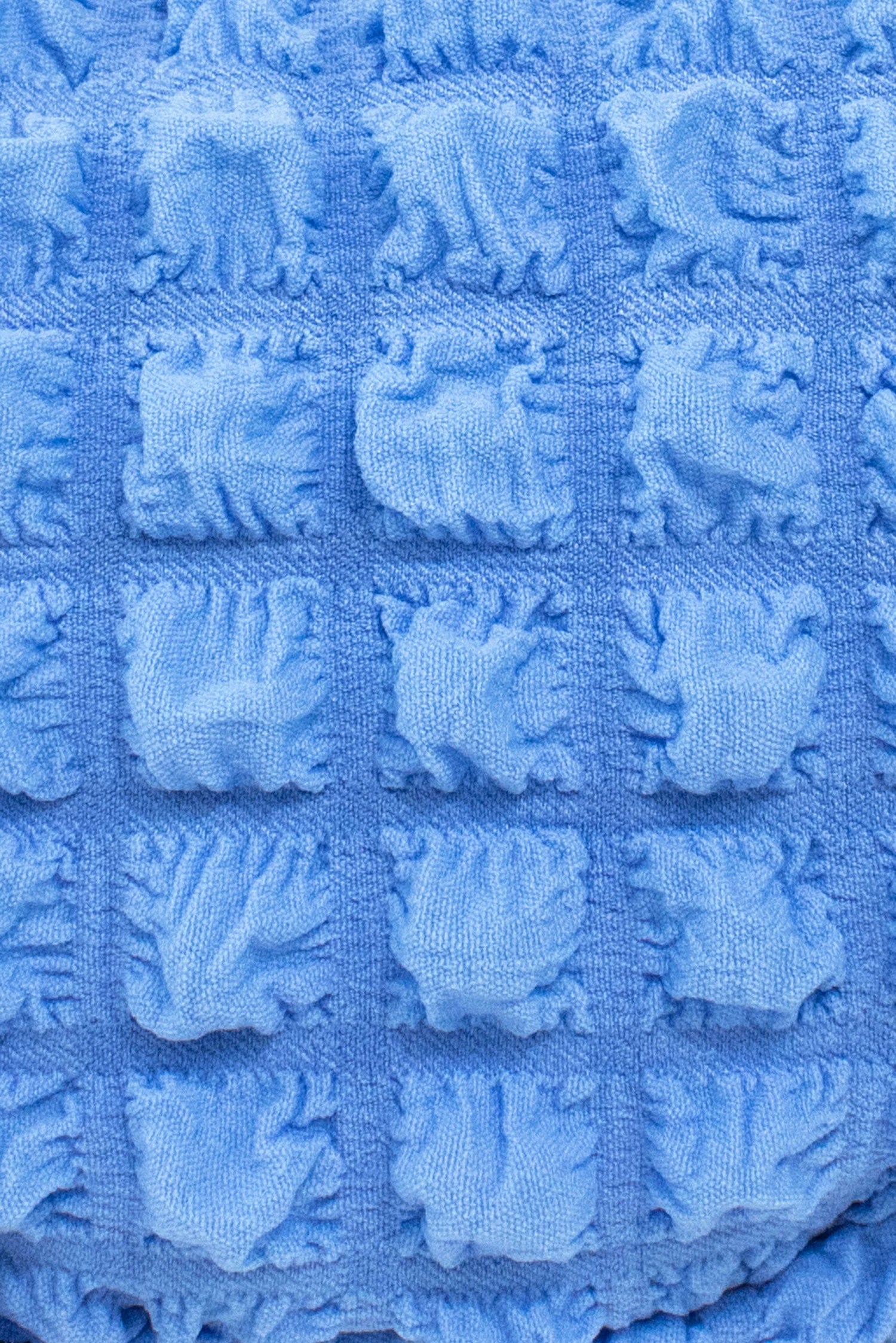 Close-up of textured light blue fabric with a repeating pattern of raised, flower-like shapes.