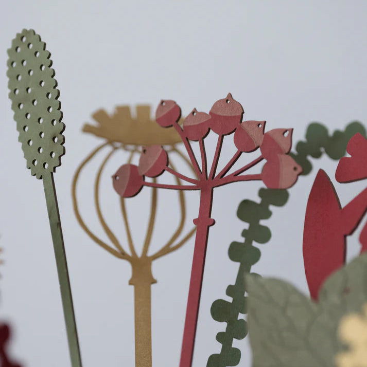 Close-up of decorative plant cutouts in red, green, and gold on a white background