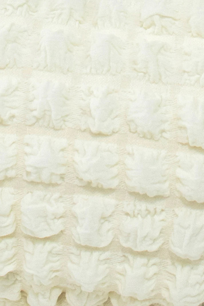 Close-up of off-white textured fabric with a repeating, raised floral pattern.
