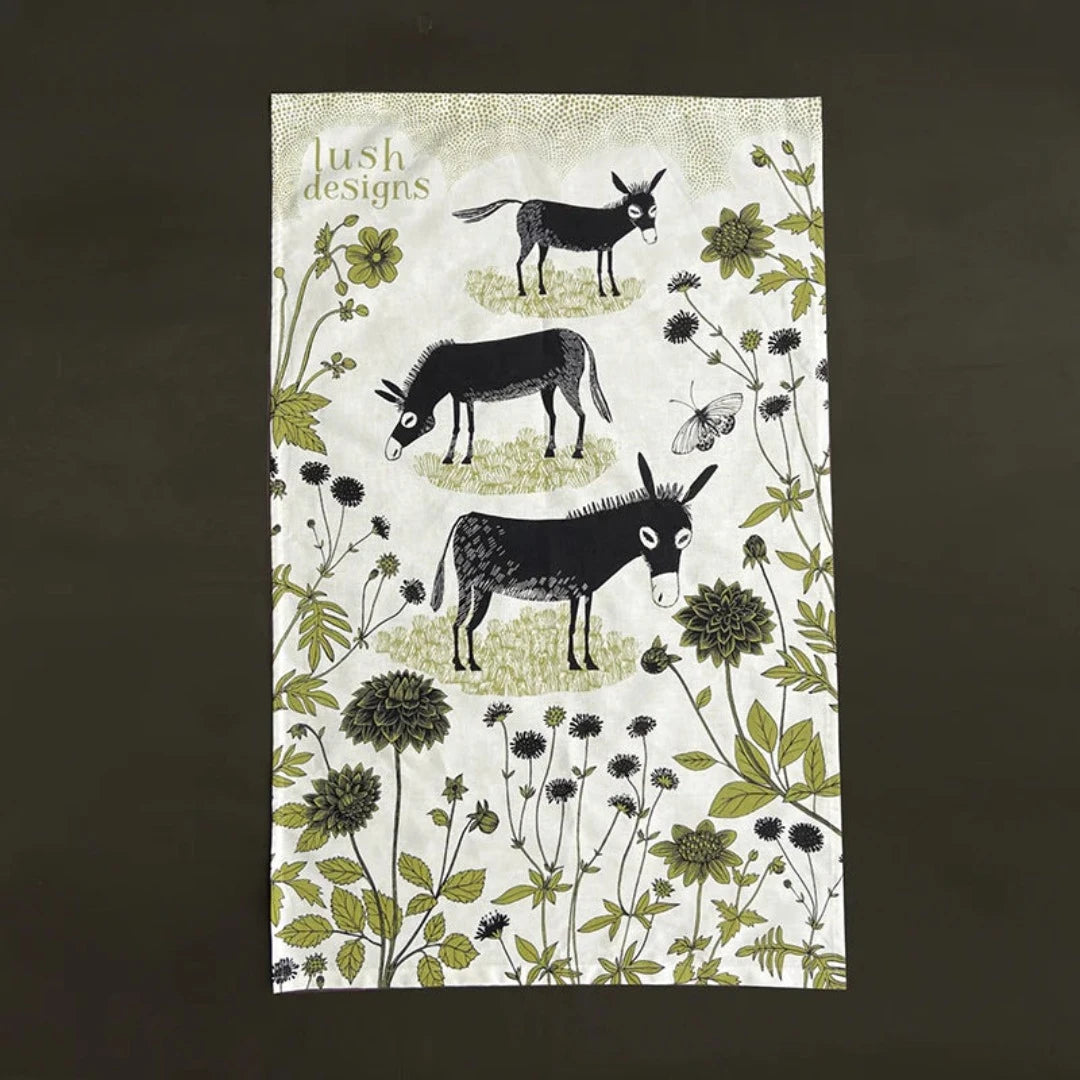 Lush Designs tea towel featuring three black donkeys and green floral illustration on an off-white background.