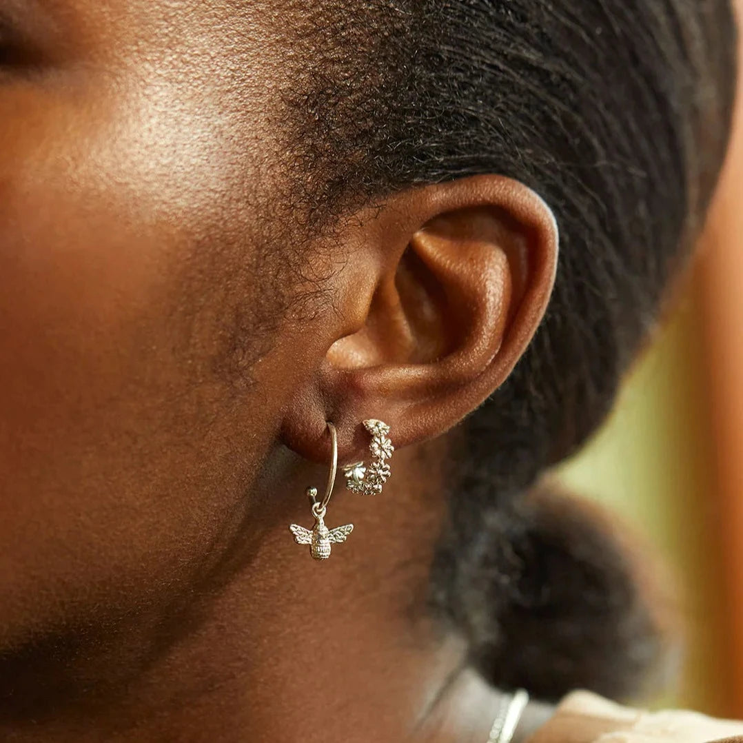 Silver bee charm hoop earrings and floral half-hoop earrings.