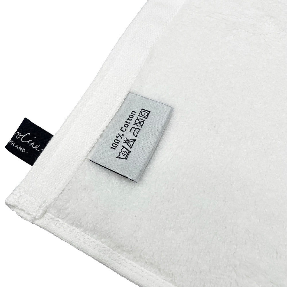 White 100% cotton towel with a sewn-in care label showing washing instructions.